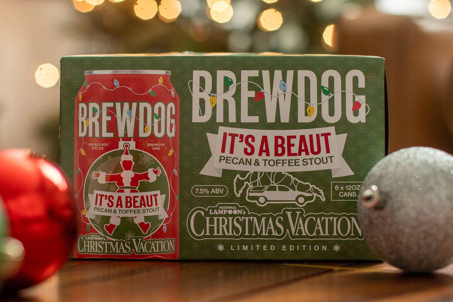 Drink 桌布 壁紙 — 一個充滿節日氣氛的BrewDog Christmas Vacation啤酒盒和罐子放在木桌上，旁邊有紅色和銀色的裝飾品，背景是溫暖的散景燈光。