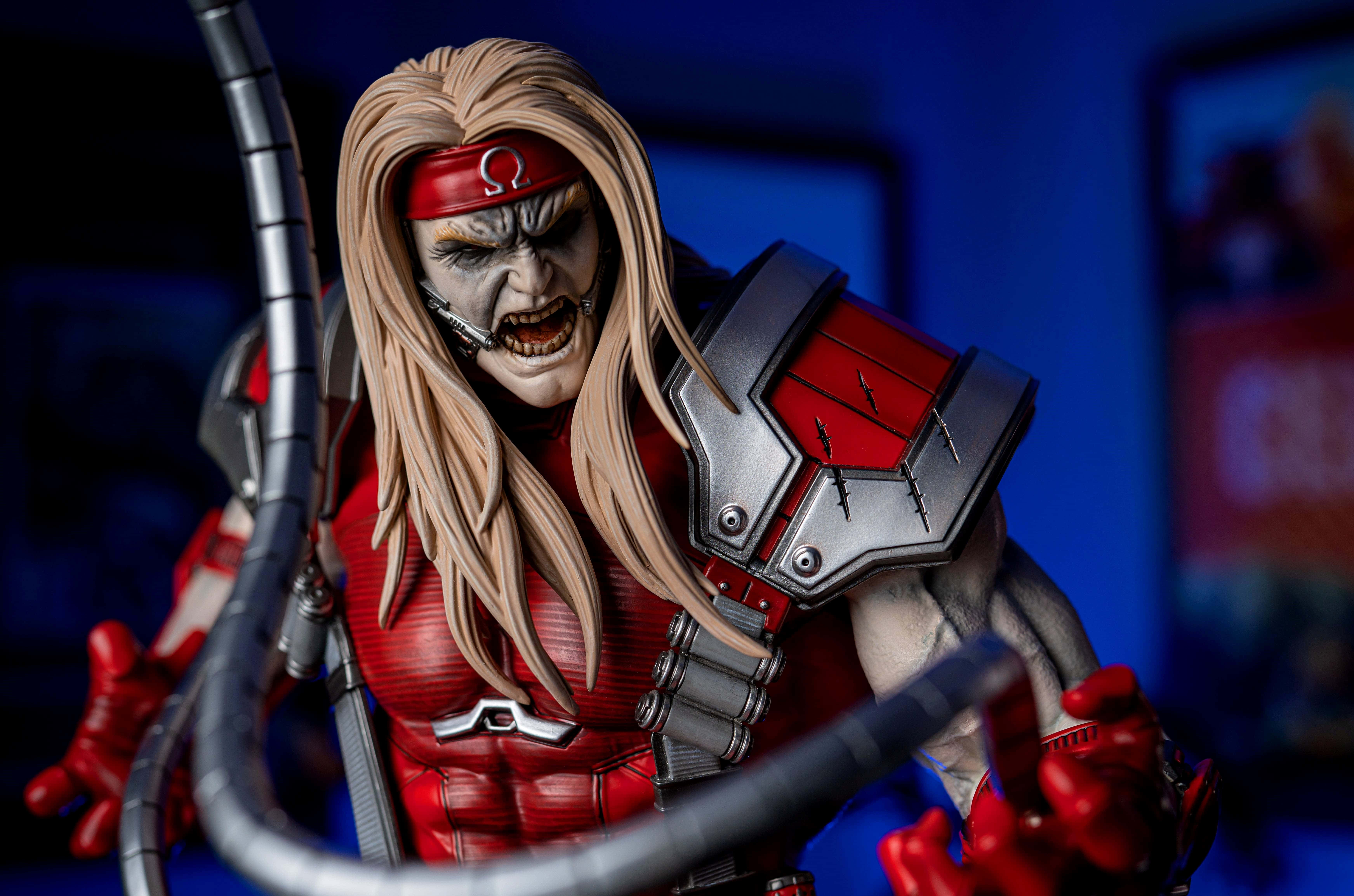 Omega Red 桌布 壁紙 — 一個兇猛的Omega Red動作人偶，長長的金色頭髮和紅色盔甲，在深藍色背景上兇狠地咆哮。