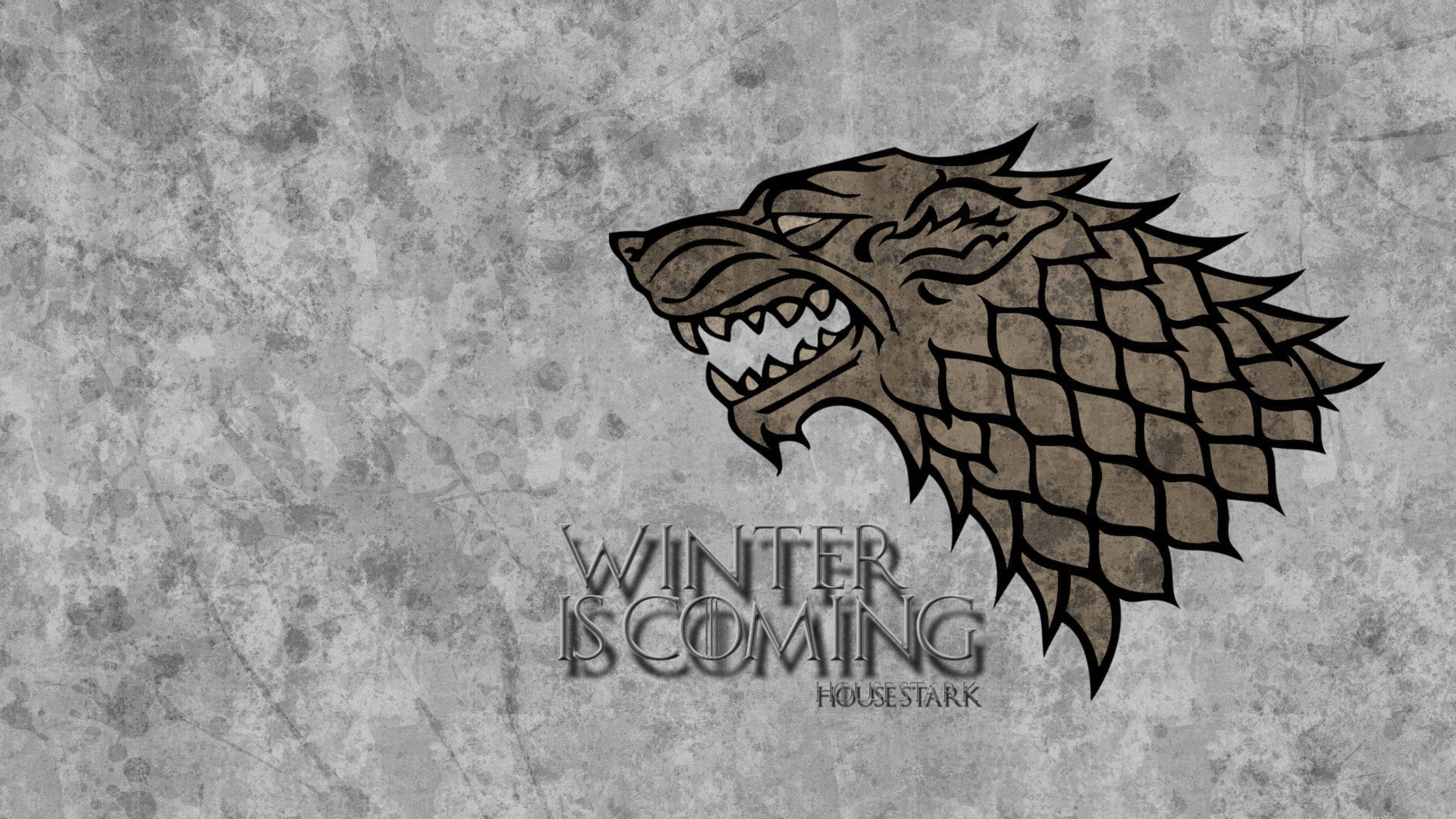 House Stark 桌布 壁紙 — 一個兇猛的冰原狼頭標誌，上面有「Winter is Coming」文字，背景是粗糙紋理的灰色。