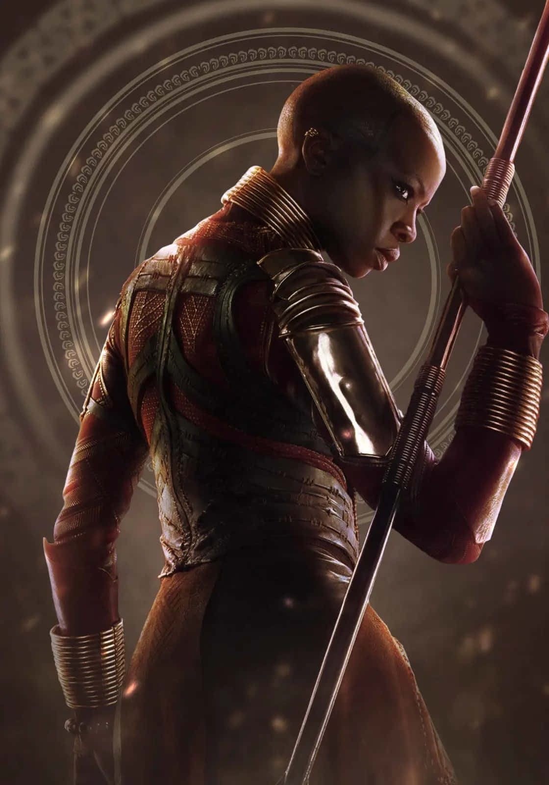 Okoye 桌布 壁紙 — 一個兇猛的戰士身穿華麗的紅色和金色盔甲，手持長矛，背景是圓形圖案。