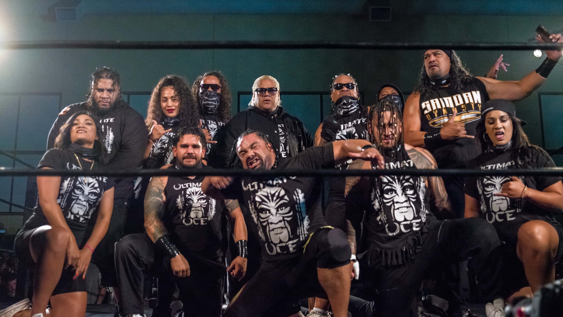 WWE 桌布 壁紙 — 一個兇猛的摔角派系自信地在擂台上擺姿勢，穿著搭配的黑色襯衫，上面有部落面具標誌。