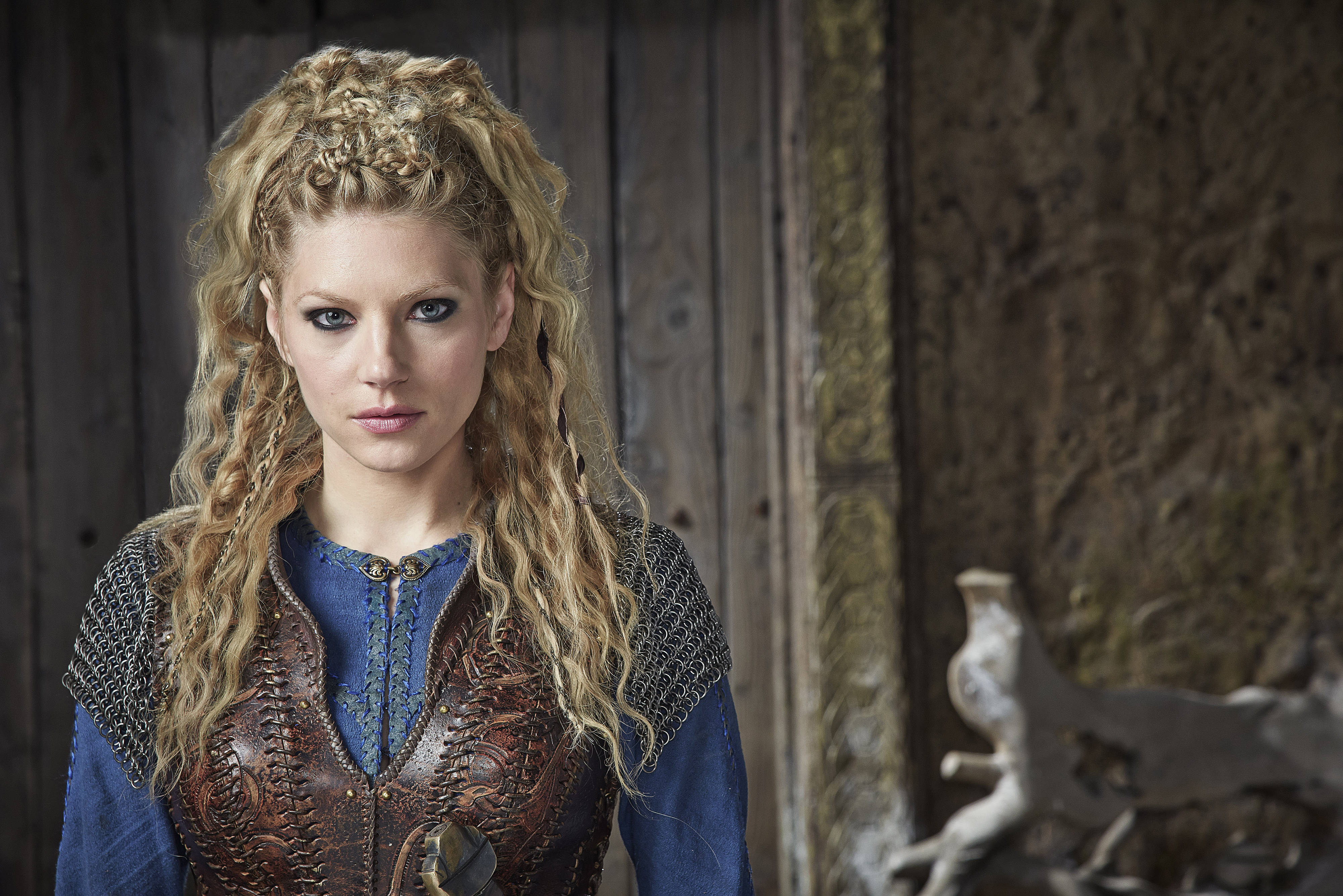Vikings 桌布 壁紙 — 一個兇猛的維京女人，編著金色辮子，在質樸的木製大廳中凝視著。