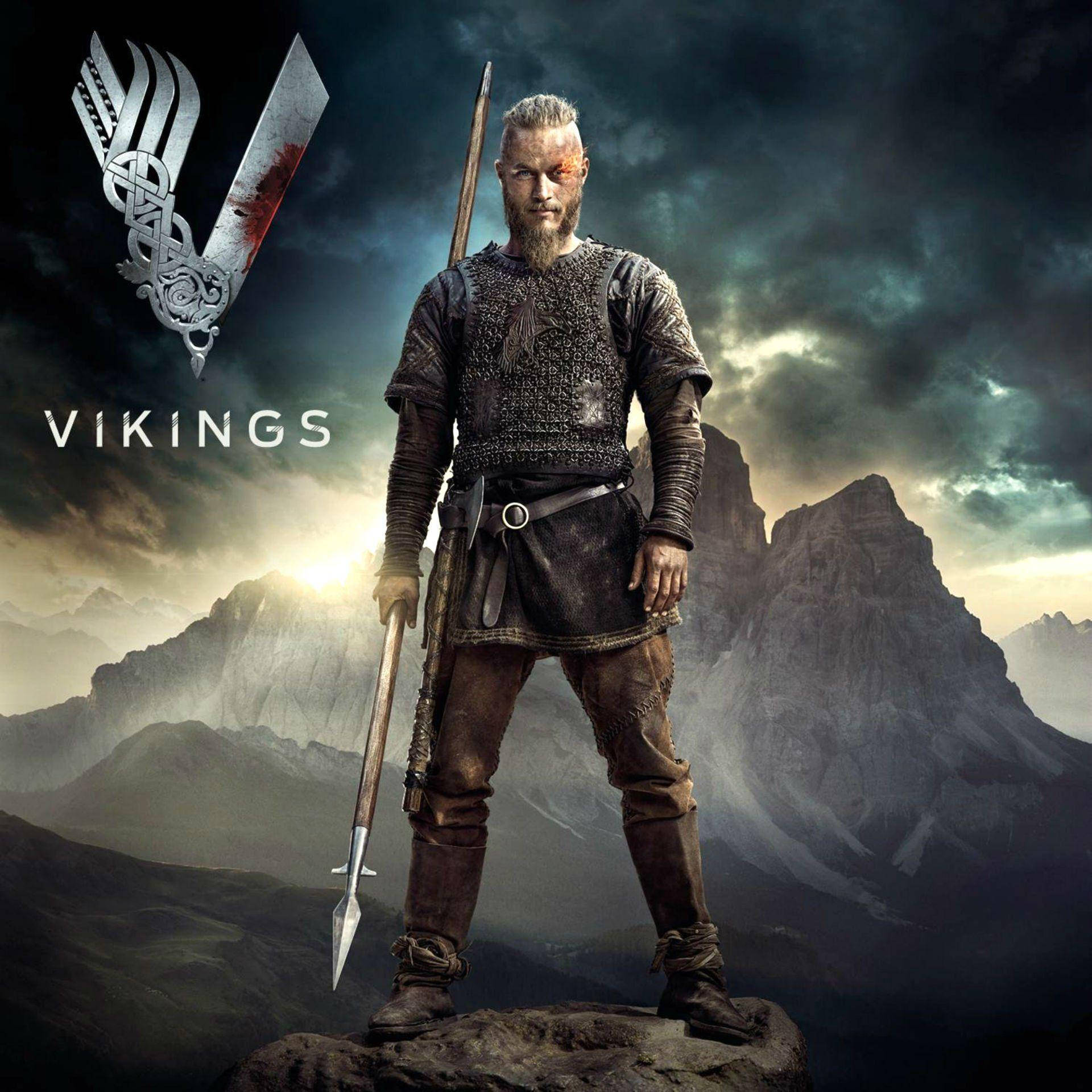 Vikings 桌布 壁紙 — 一個兇猛的維京戰士站在岩石山頂上，手持長矛，背景是暴風雨的山脈，並帶有血跡斑斑的斧頭標誌。