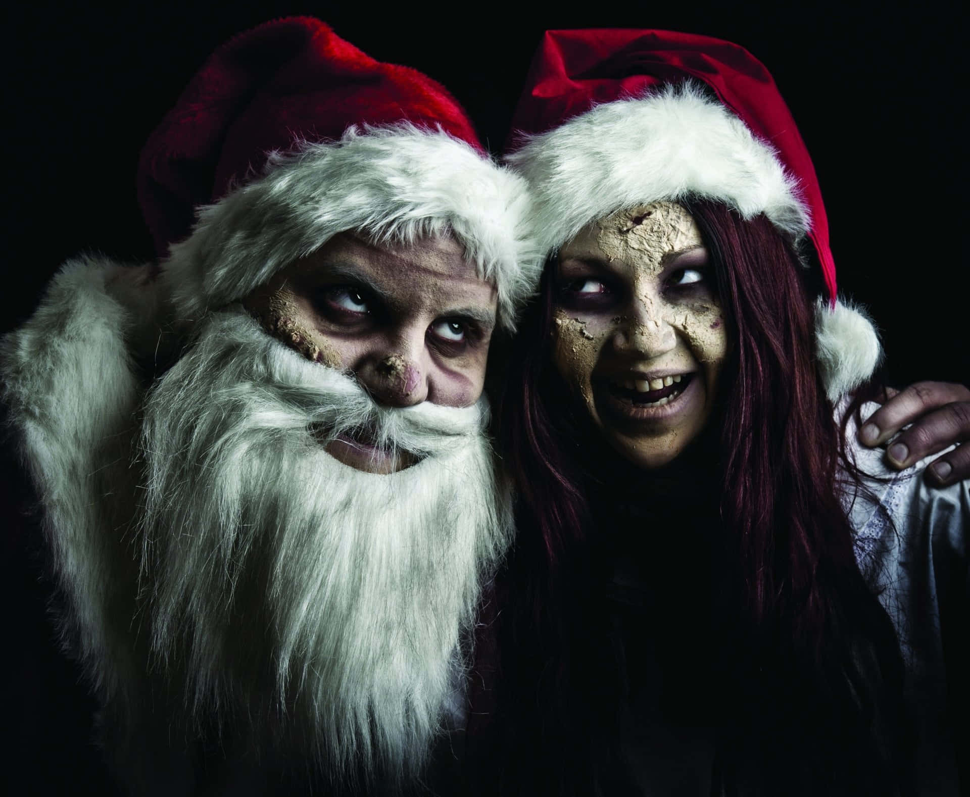 Santa 桌布 壁紙 — 一個兇神惡煞的聖誕老人和一個戴著聖誕帽的殭屍女人在黑色背景前咧嘴笑。
