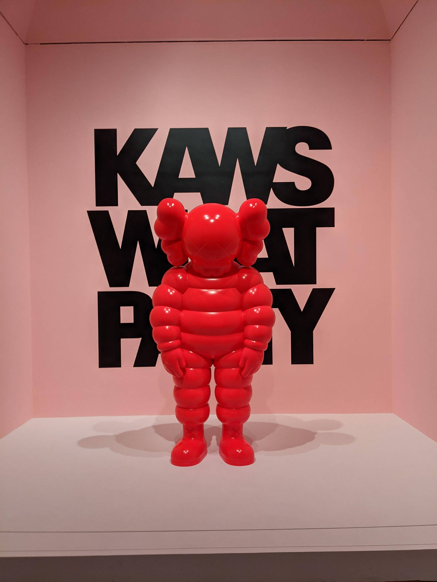 kaws pc 桌布 壁紙 — 一個光滑的紅色KAWS Companion雕塑矗立在白色底座上，背景是粉紅色的牆壁，上面有粗體黑色文字「KAWS WHAT PARTY」。