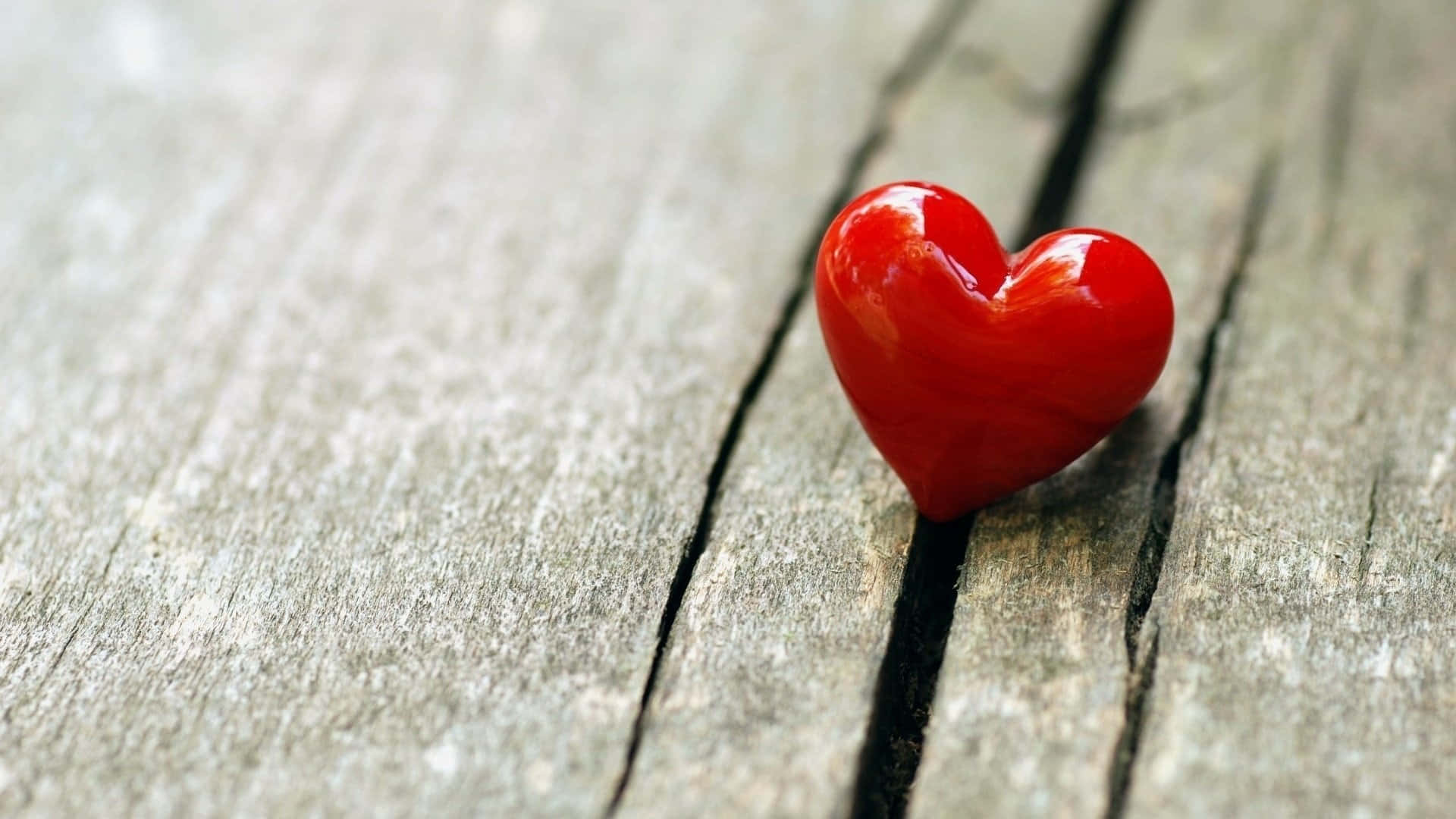 Red Heart 桌布 壁紙 — 一個光滑的紅色心形物體放在有深裂縫的風化灰色木板上。