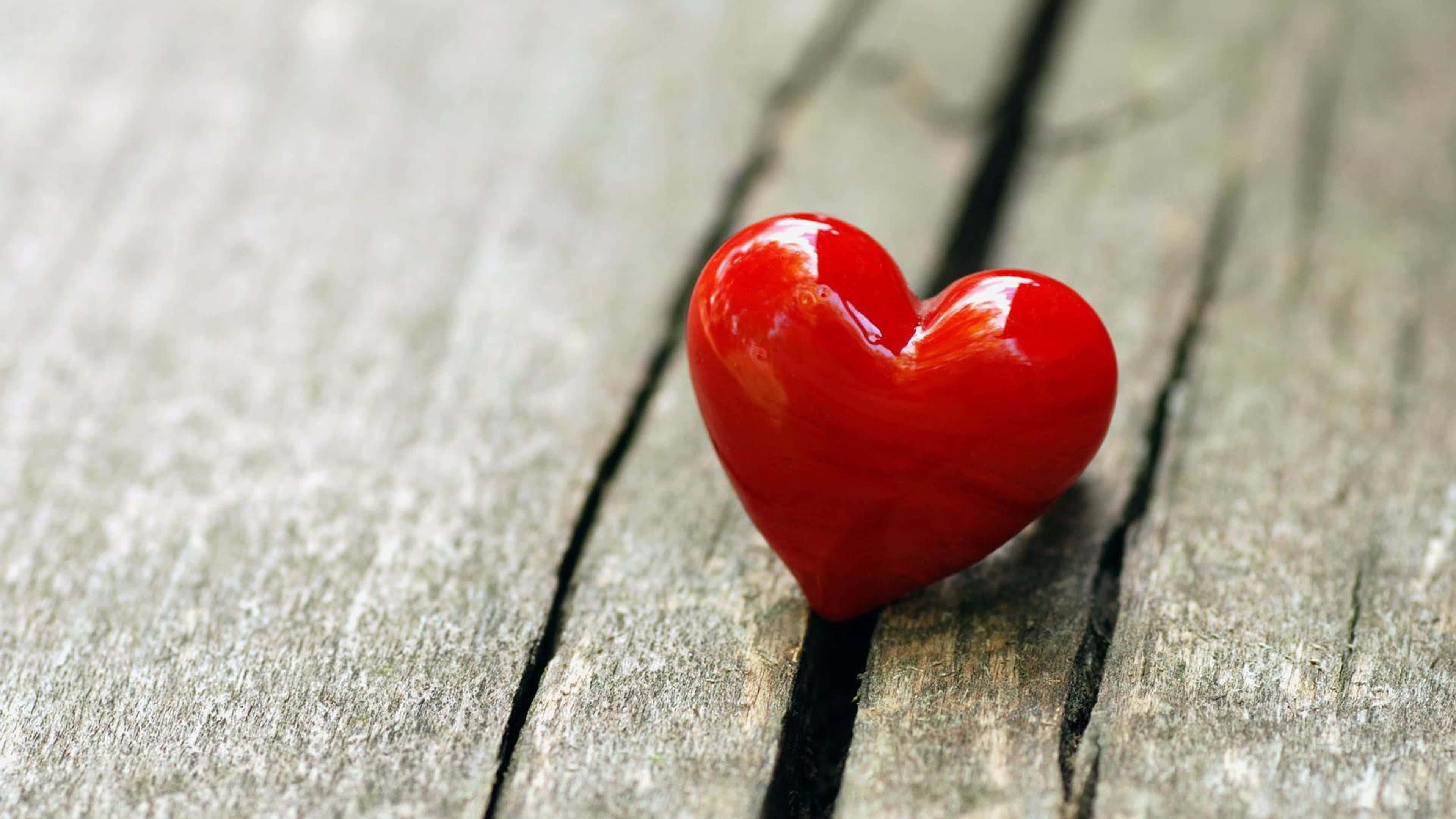 4K Love 桌布 壁紙 — 一個光滑的紅色心形物體放置在帶有可見裂縫的風化灰色木板上。