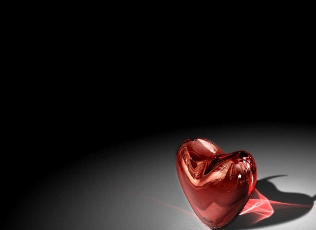 Red Heart 桌布 壁紙 — 一個光滑的紅色心形玻璃物體放置在深色表面上，戲劇性的燈光投射出柔和的陰影。