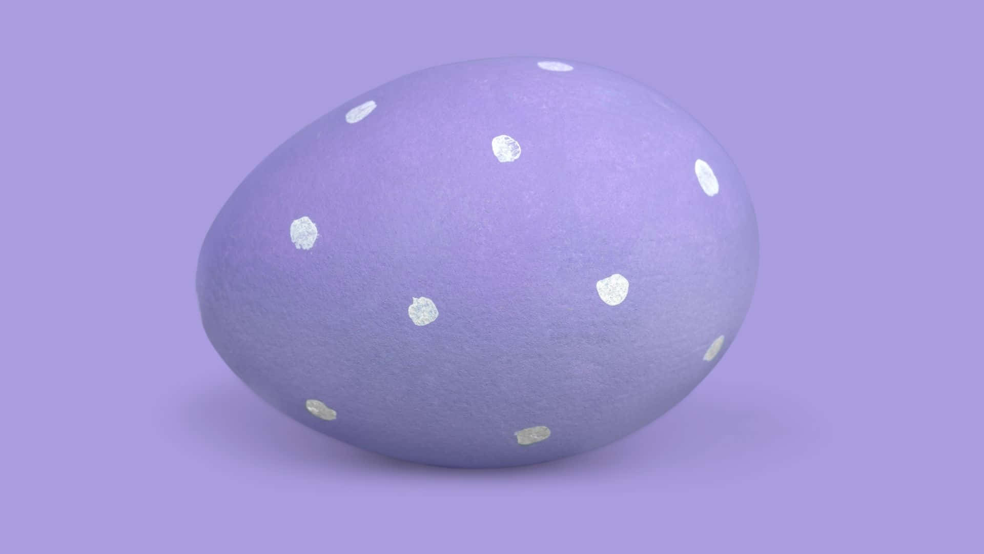 Easter Egg 桌布 壁紙 — 一個光滑的薰衣草色雞蛋，上面散落著白色圓點，靠在純色薰衣草背景上。