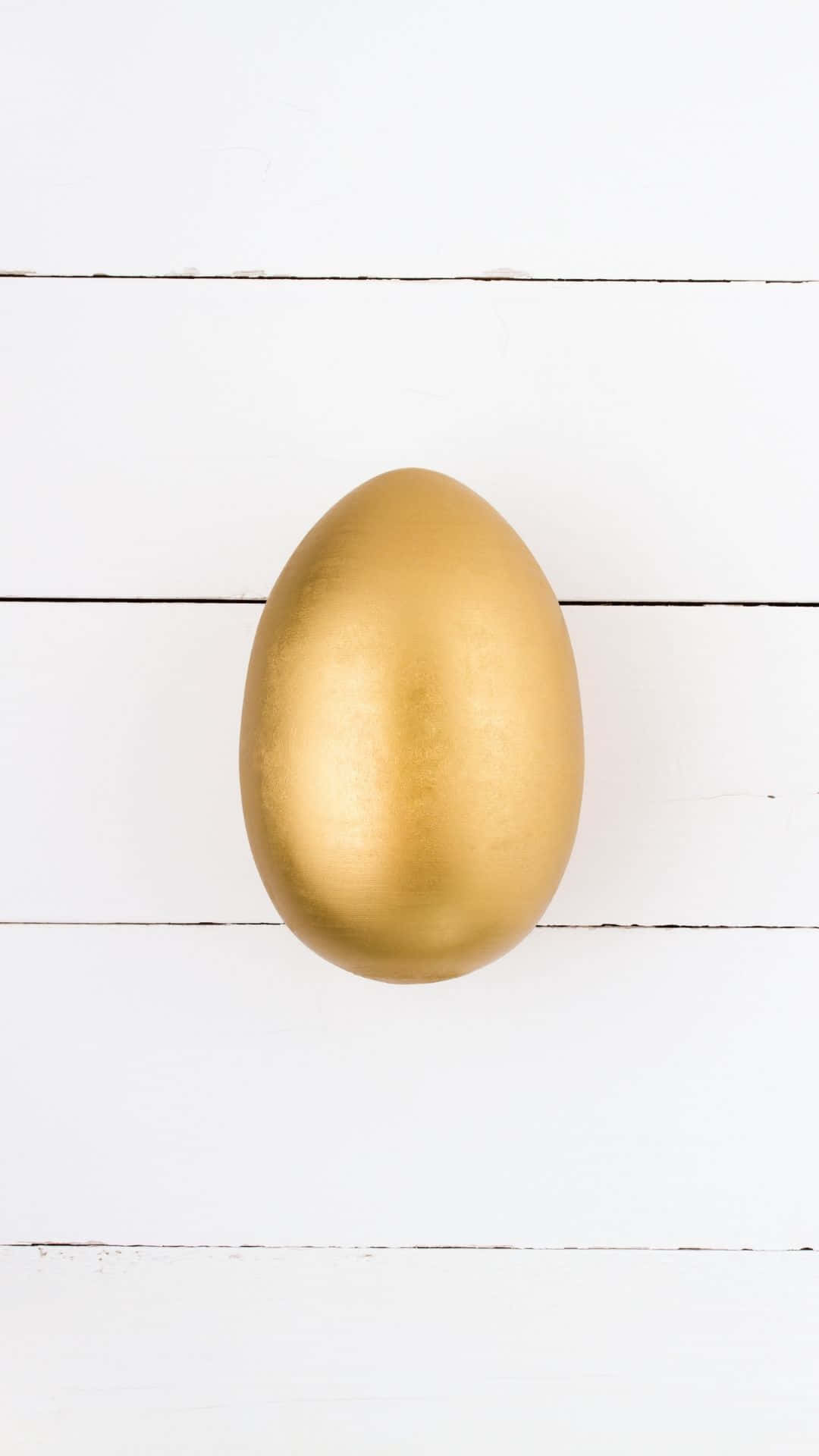 Easter Egg 桌布 壁紙 — 一個光滑的金色雞蛋置於白色木板上，在柔和均勻的光線下居中擺放。
