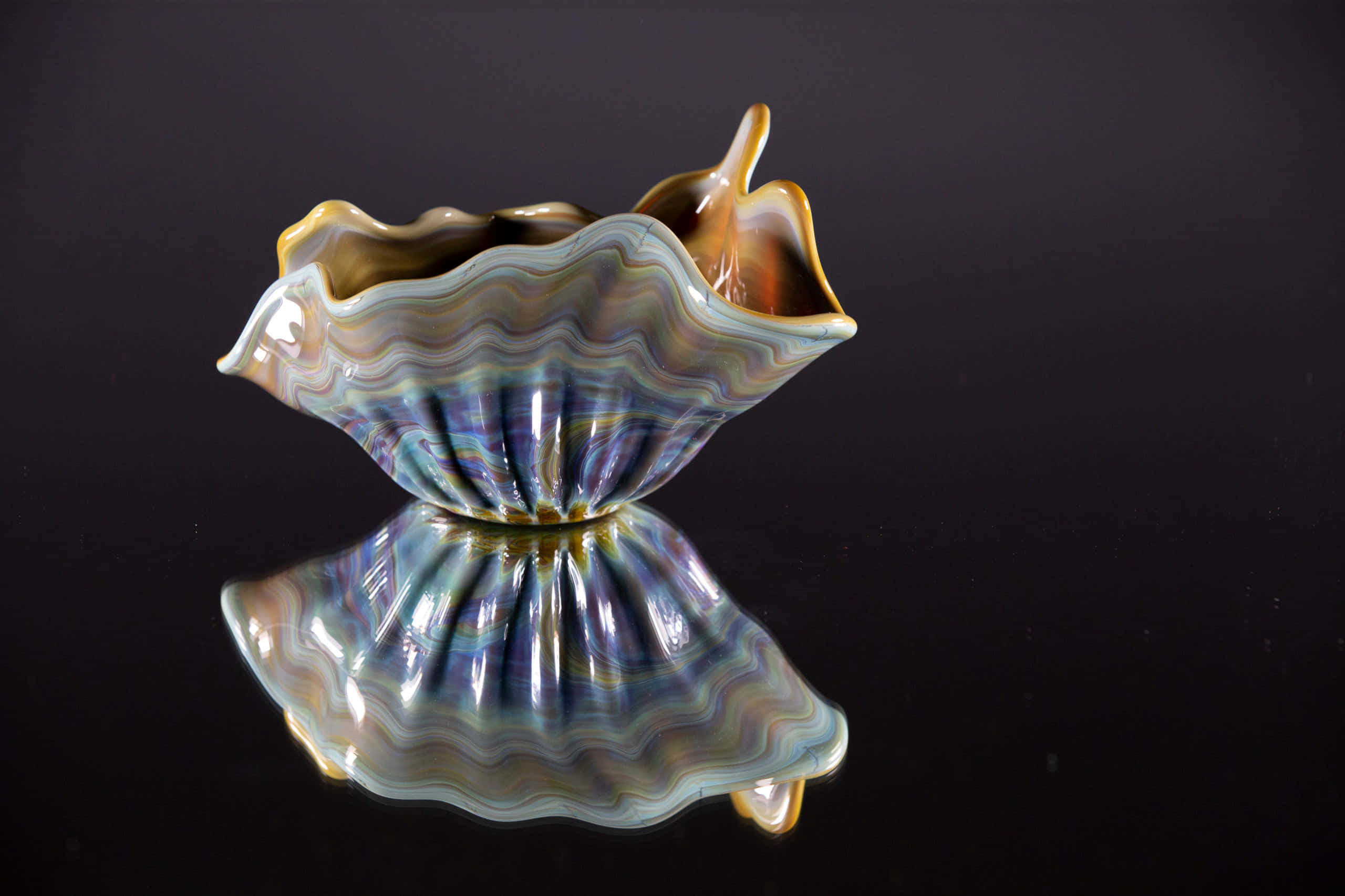 Clam Shell 桌布 壁紙 — 一個光滑的陶瓷貝殼形碗，帶有藍色、紫色和金色的虹彩漩渦，放置在反光的黑色表面上。
