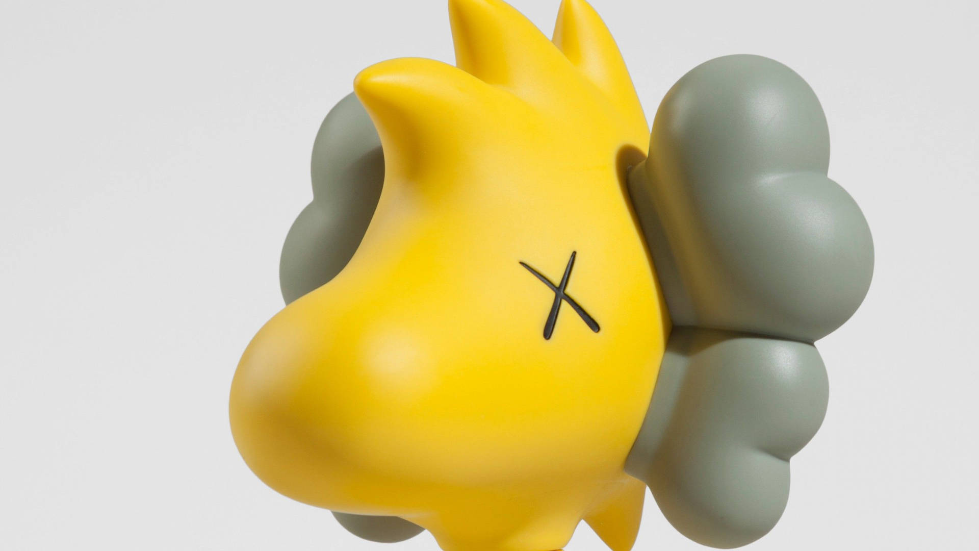 kaws pc 桌布 壁紙 — 一個光滑的黃色太陽雕塑，帶有黑色X形臉和灰色煙霧狀附屬物，背景為純白色。