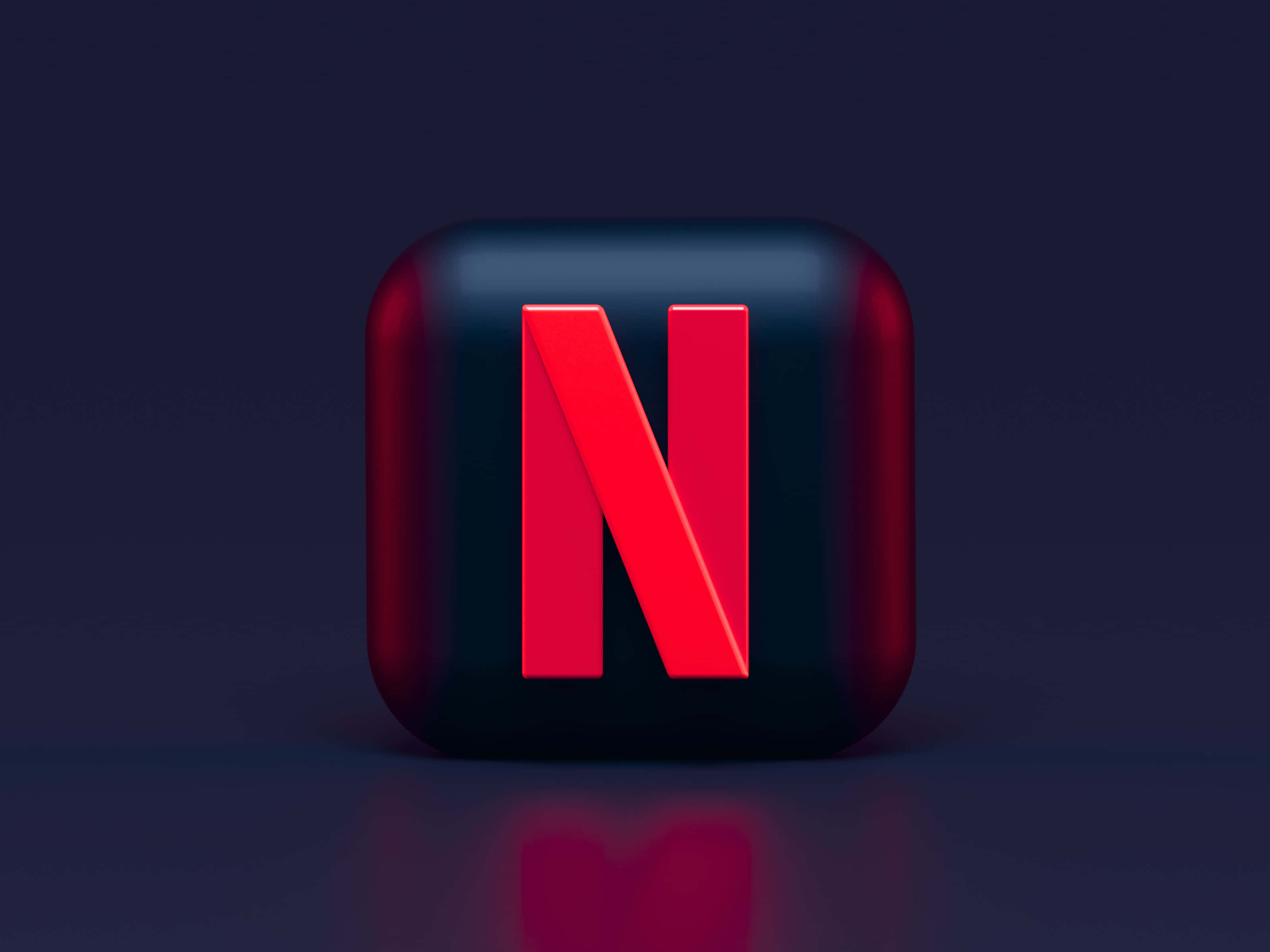 Netflix 桌布 壁紙 — 一個光滑的黑色立方體，帶有醒目的紅色Netflix標誌，置於深色反光表面上，在柔和的工作室燈光下居中。