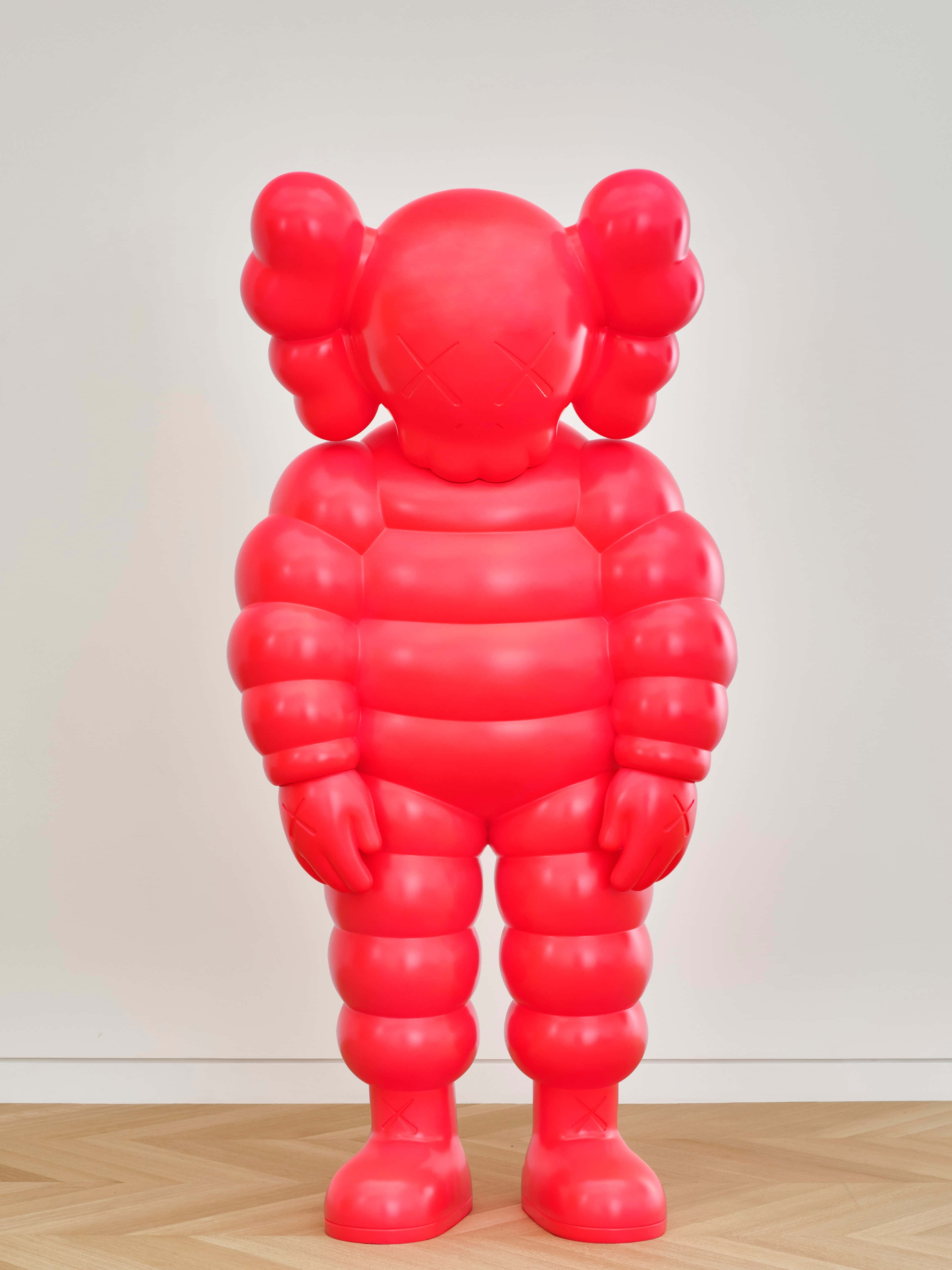 KAWS 桌布 壁紙 — 一個光澤亮麗的紅色KAWS Companion雕塑高高地立在木地板上，背景是純白牆壁。