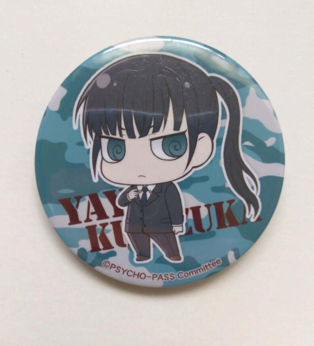 Yayoi Kunizuka 桌布 壁紙 — 一個光澤動漫風格鈕扣徽章，上面有《PSYCHO-PASS 心靈判官》的黃泉月彌生Q版角色穿著校服，背景為藍色迷彩。