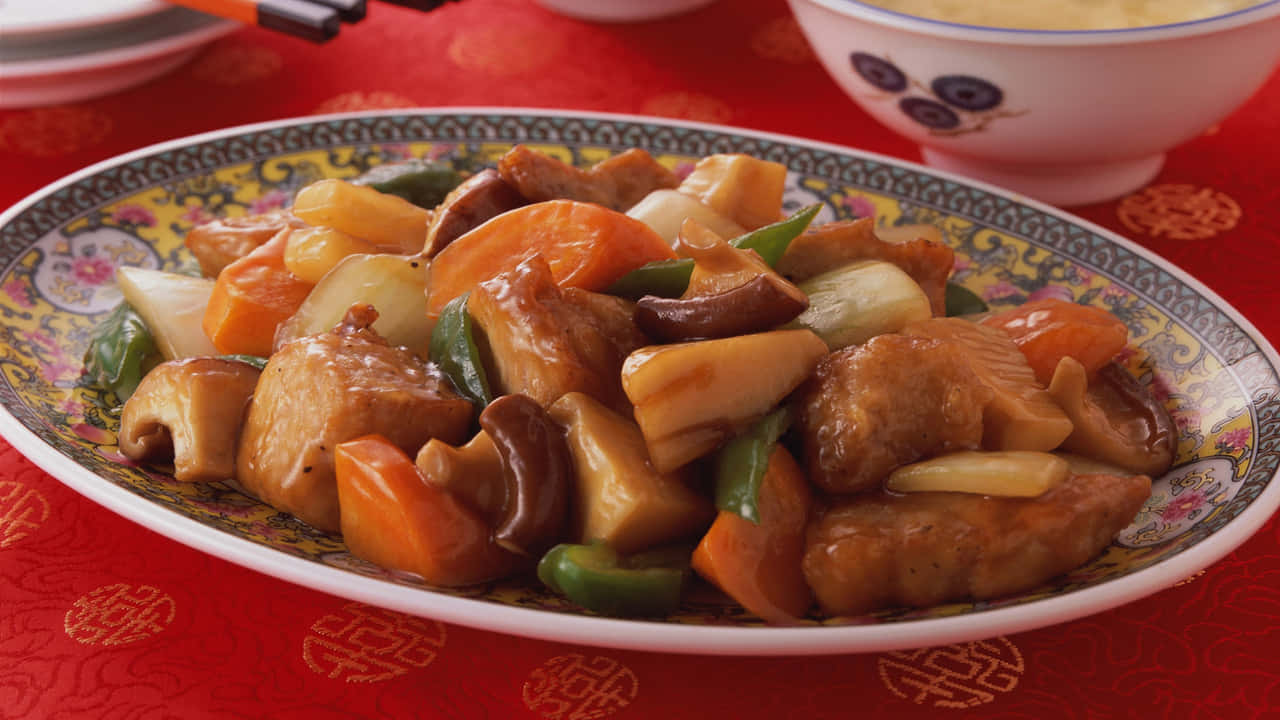 720p Food 桌布 壁紙 — 一個光澤的雞肉、蘑菇和蔬菜炒菜，放在一個花卉圖案的盤子上，置於紅色圖案桌布上。