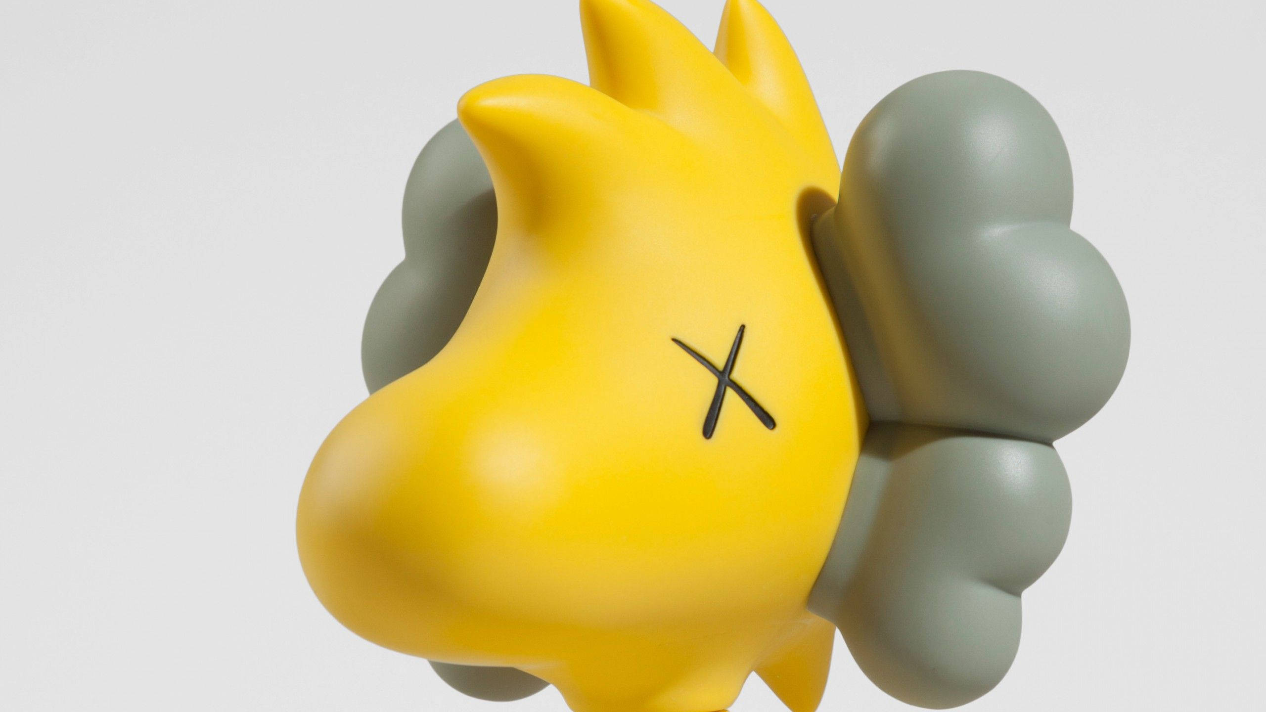 KAWS 桌布 壁紙 — 一個光澤的黃色太陽雕塑，帶有黑色X眼睛和灰色煙霧狀翅膀，背景為純白色。