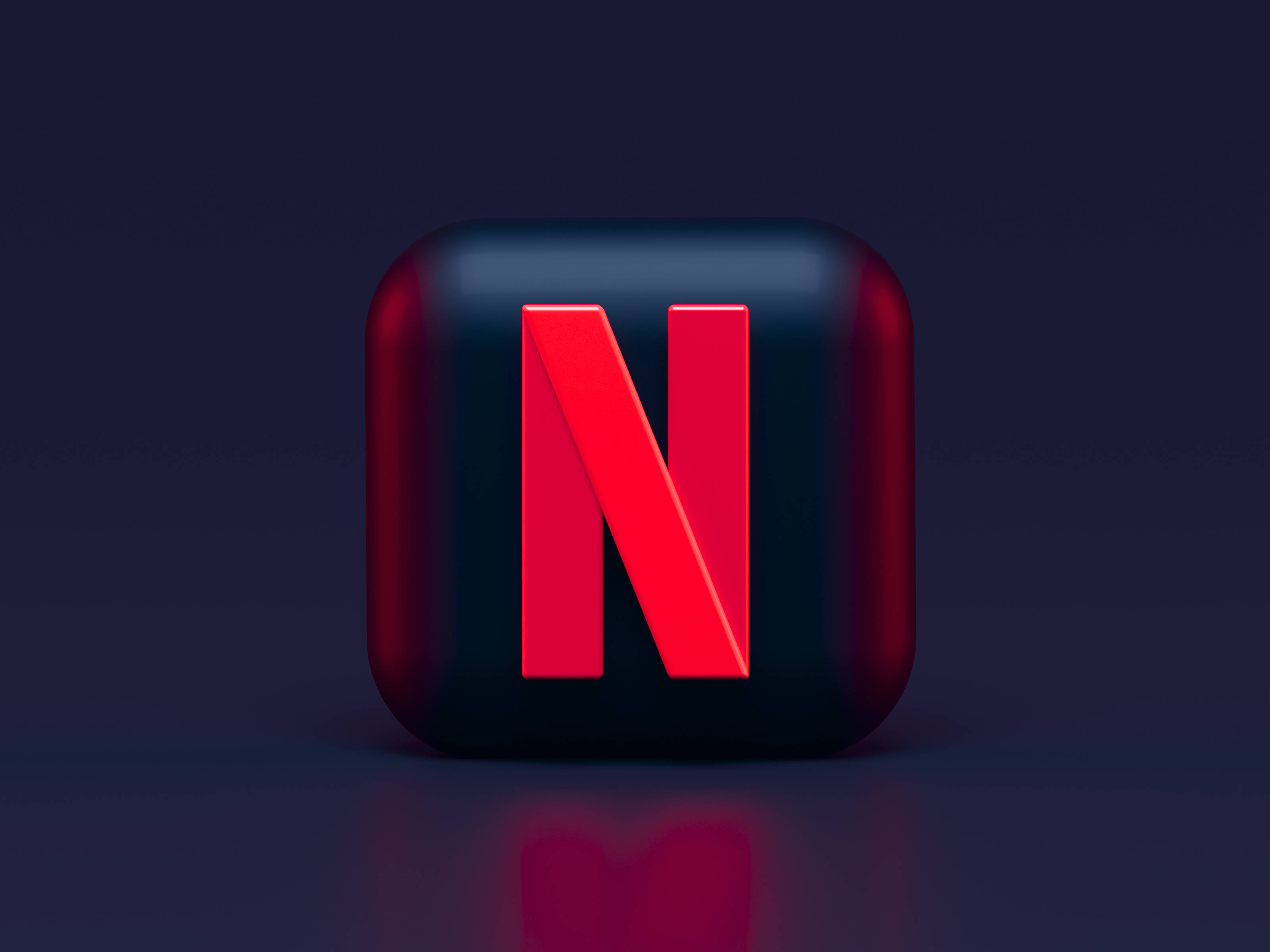 Netflix 桌布 壁紙 — 一個光澤的黑色立方體，帶有醒目的紅色Netflix標誌，在工作室燈光下居中放置在深色反光表面上。