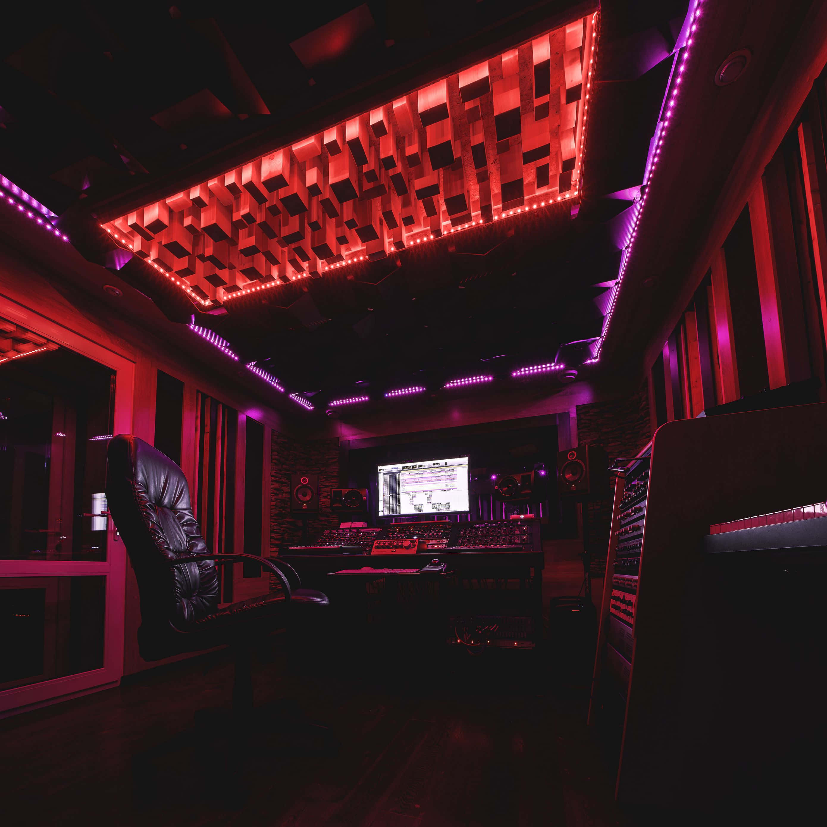 Studio 桌布 壁紙 — 一個光線昏暗的專業錄音室，沐浴在紅色和紫色的LED燈光中，配有隔音板和混音控制台。