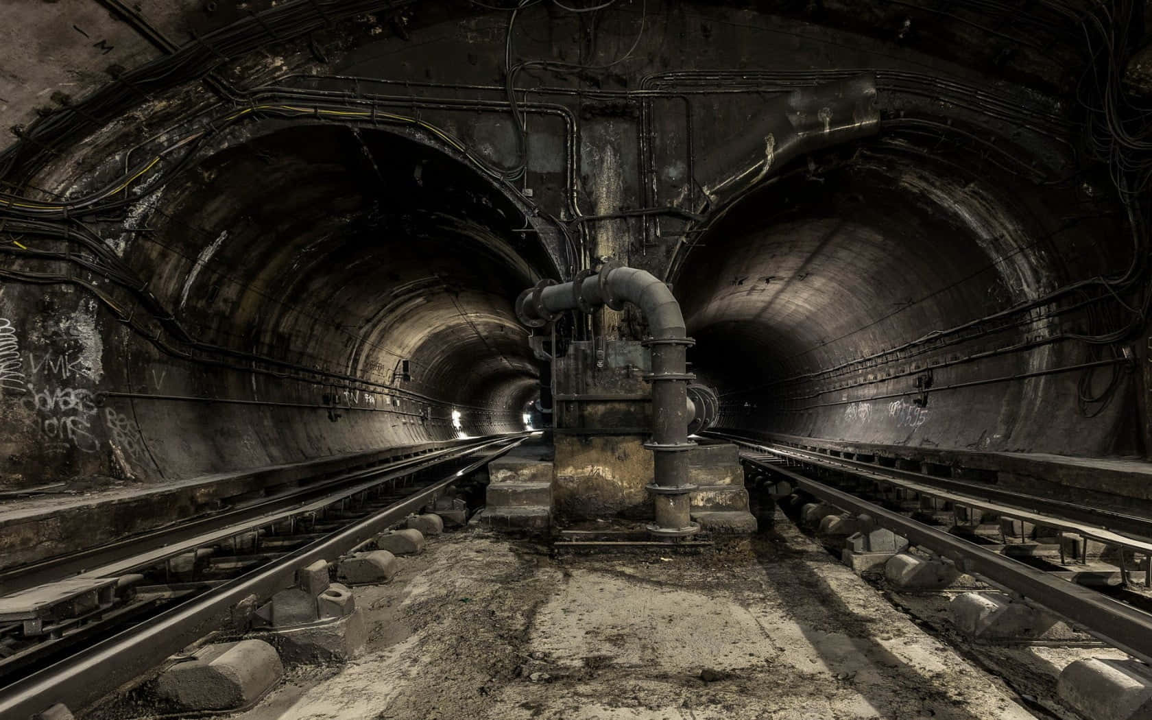 Dark Underground 桌布 壁紙 — 一個光線昏暗的廢棄地鐵隧道，生鏽的軌道、佈滿塗鴉的牆壁和暴露的管道，營造出一種粗獷的工業氛圍。