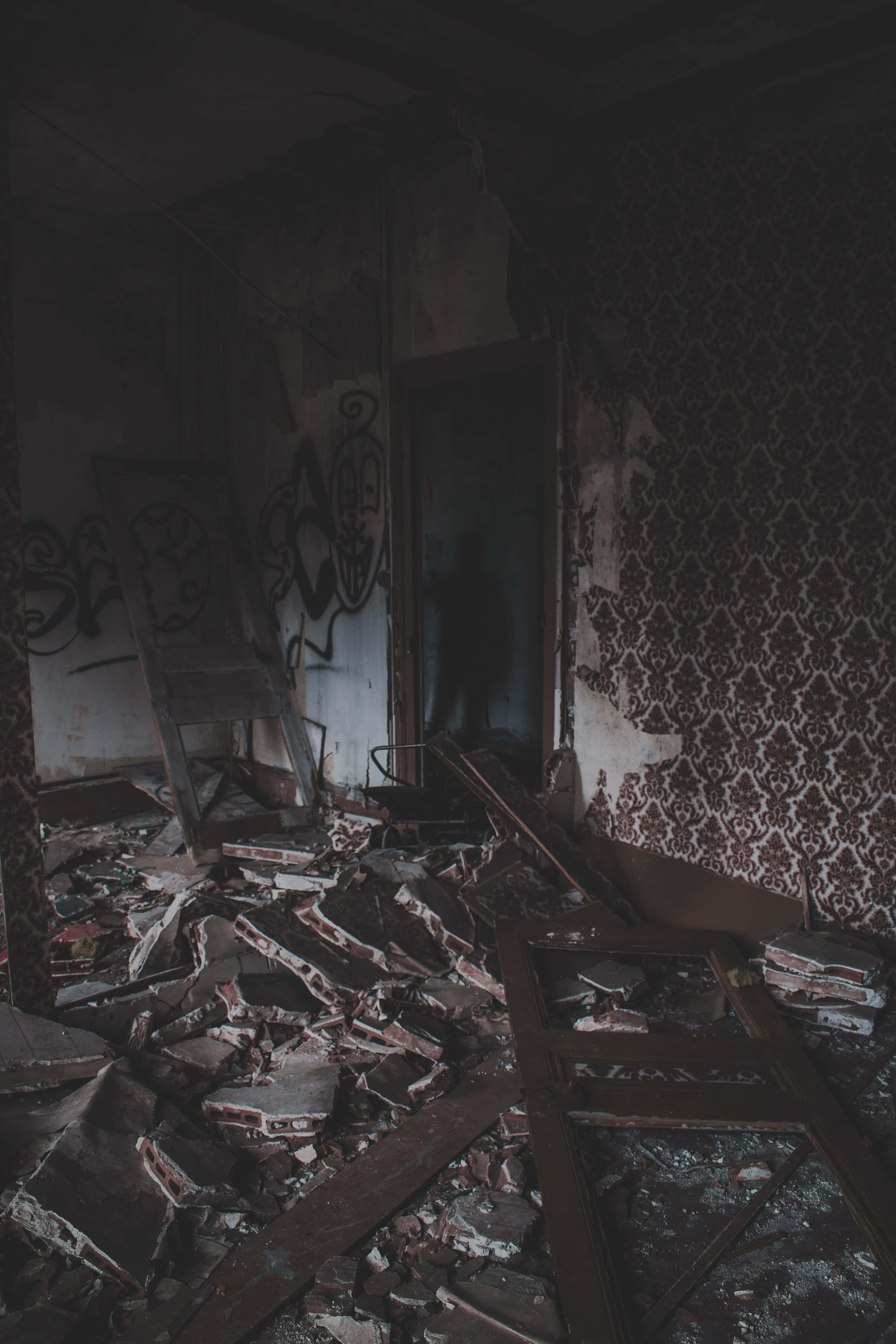haunted 桌布 壁紙 — 一個光線昏暗的廢棄房間，地板上散落著破碎的碎片，剝落的壁紙上佈滿塗鴉。