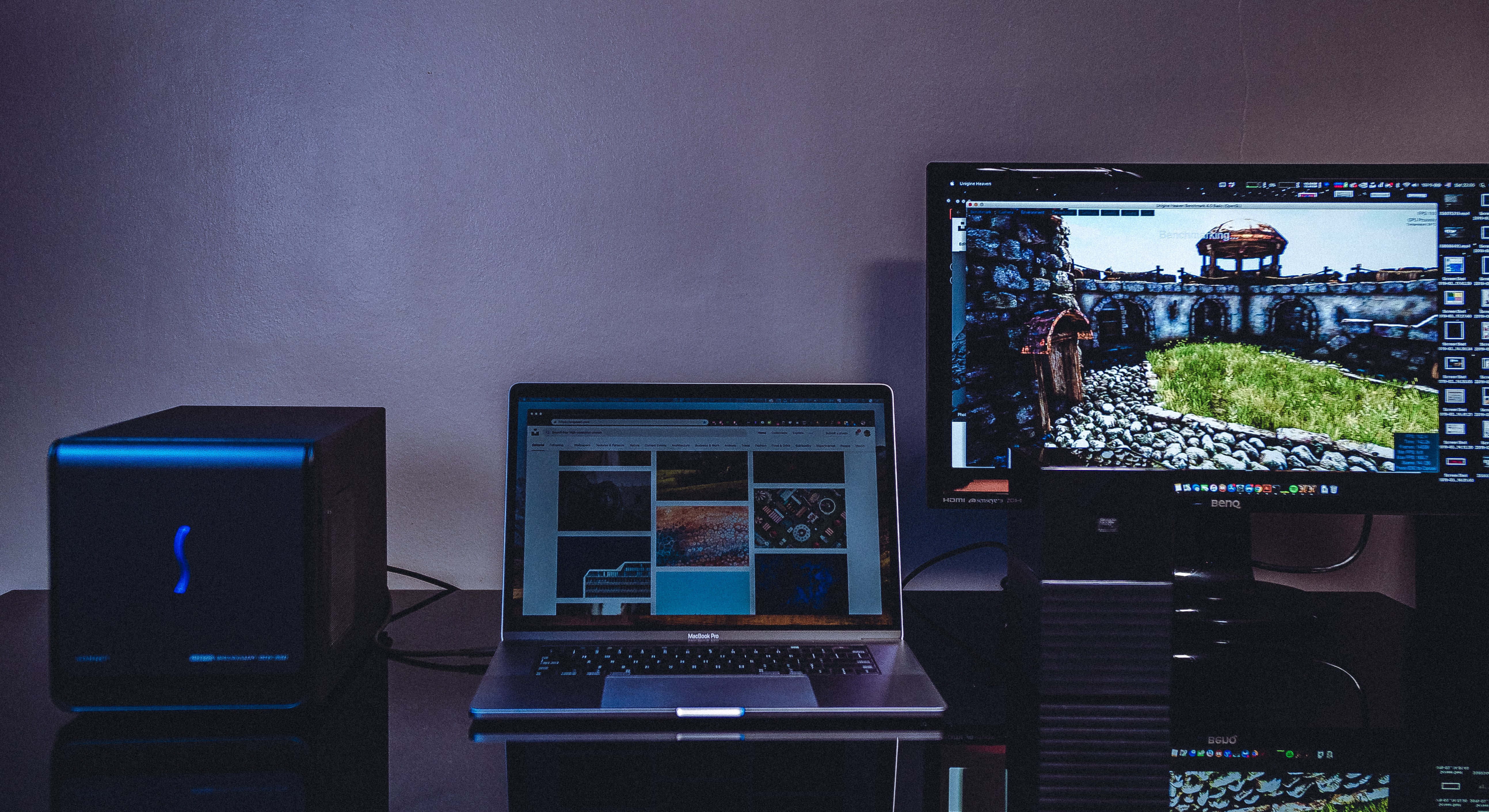 Computer Monitor 桌布 壁紙 — 一個光線昏暗的桌面設置，配備筆記型電腦和顯示器，顯示風景照片編輯軟體介面。