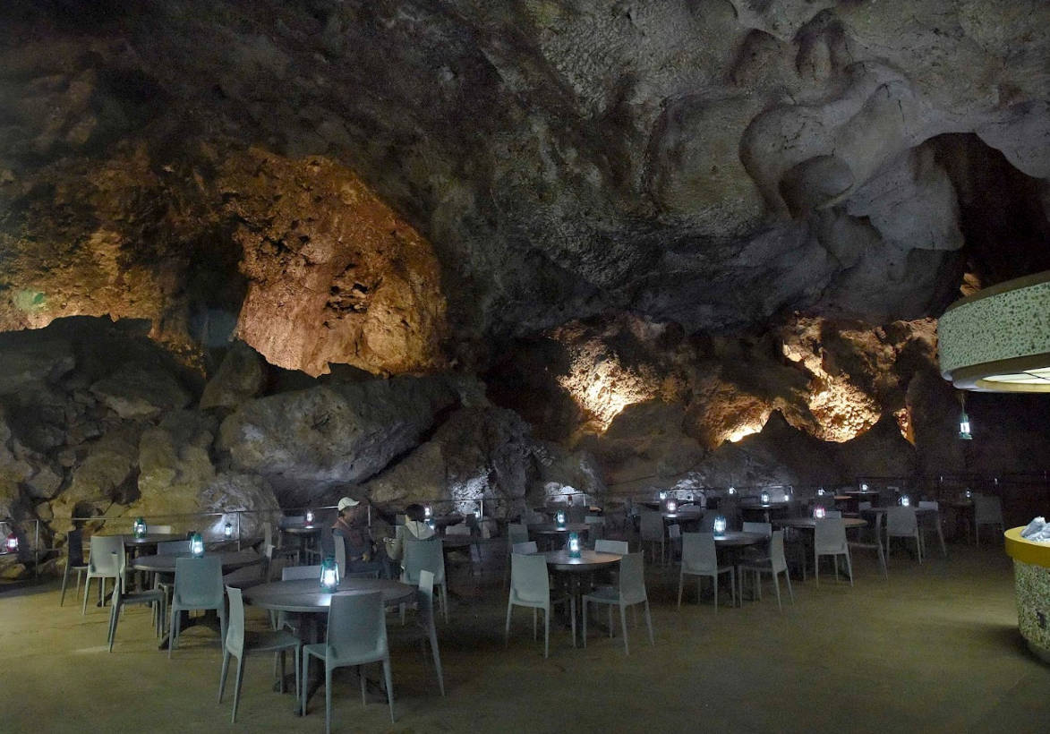 Carlsbad Caverns 桌布 壁紙 — 一個光線昏暗的洞穴餐廳，在堅固的岩石結構下設有桌椅和溫暖的燈籠。