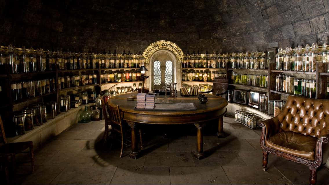 The Hogwarts Potions Class 桌布 壁紙 — 一個光線昏暗的石牆藥水房，架上擺滿裝有發光液體的玻璃罐，中央有一張木桌，上方是哥德式拱窗。