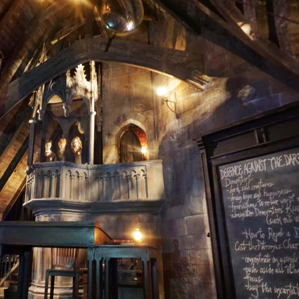 The Hogwarts Dark Arts Classroom 桌布 壁紙 — 一個光線昏暗的石頭教室，帶有哥德式拱門和黑板，上面列出了黑魔法防禦術的咒語。