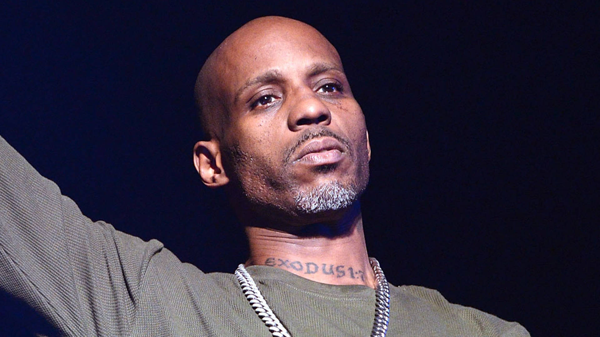 Dmx 桌布 壁紙 — 一個光頭、留山羊鬍、頸部有刺青的男人在舞台燈光下，於黑暗背景中舉起手臂。