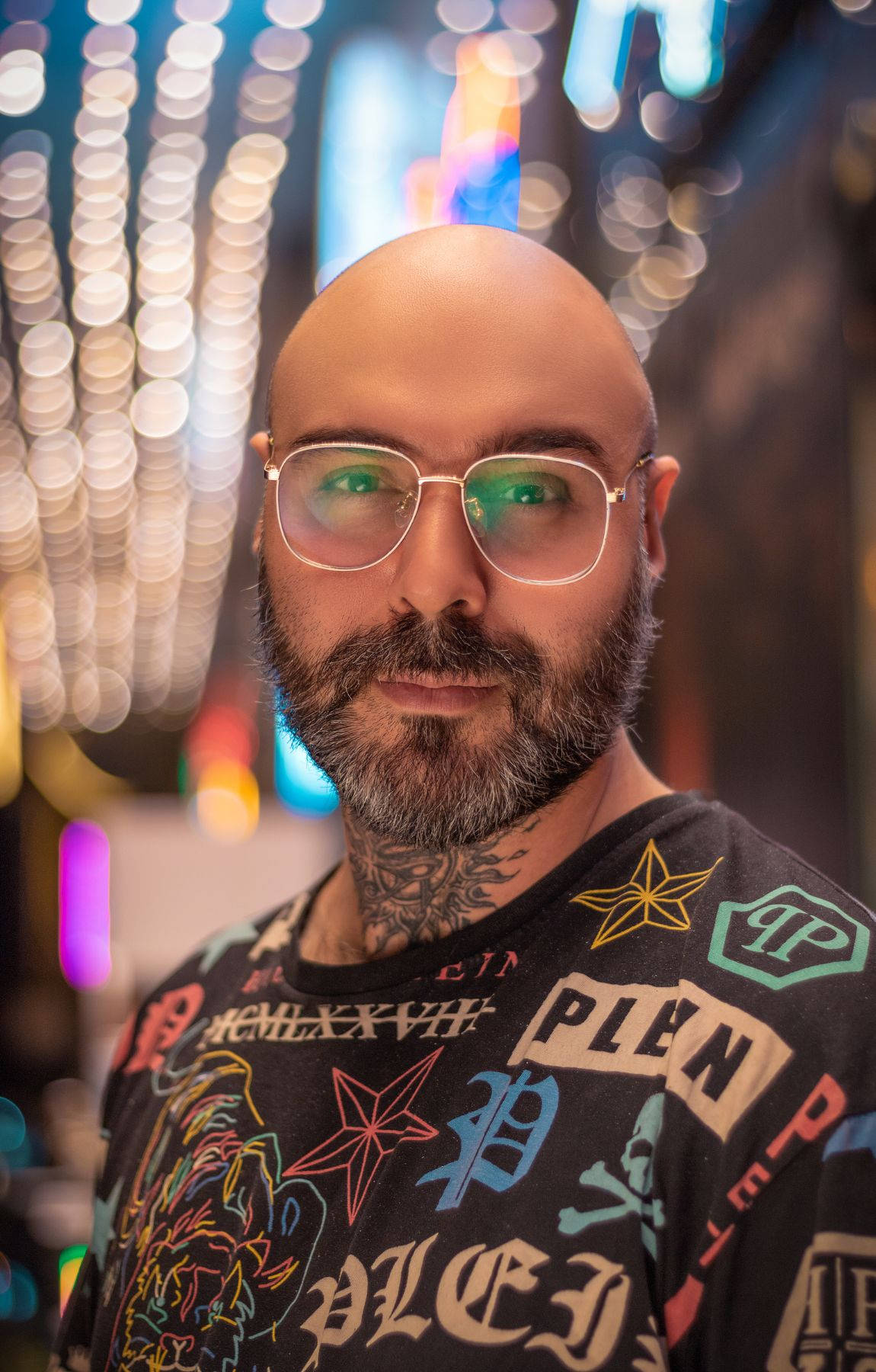 glasses 桌布 壁紙 — 一個光頭、留鬍鬚、戴眼鏡的男人站在充滿活力的霓虹燈城市夜景中，背後有散景燈光。