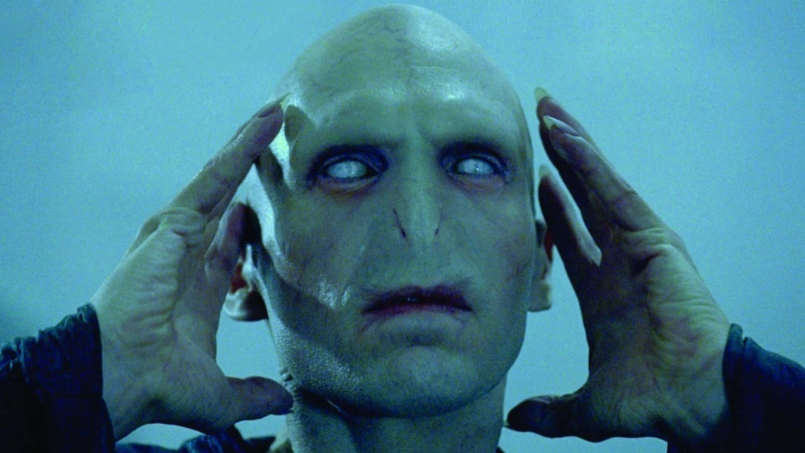 voldemort 桌布 壁紙 — 一個光頭、蒼白皮膚、大眼睛的男人，在清涼的藍色背景前用雙手抱著頭。