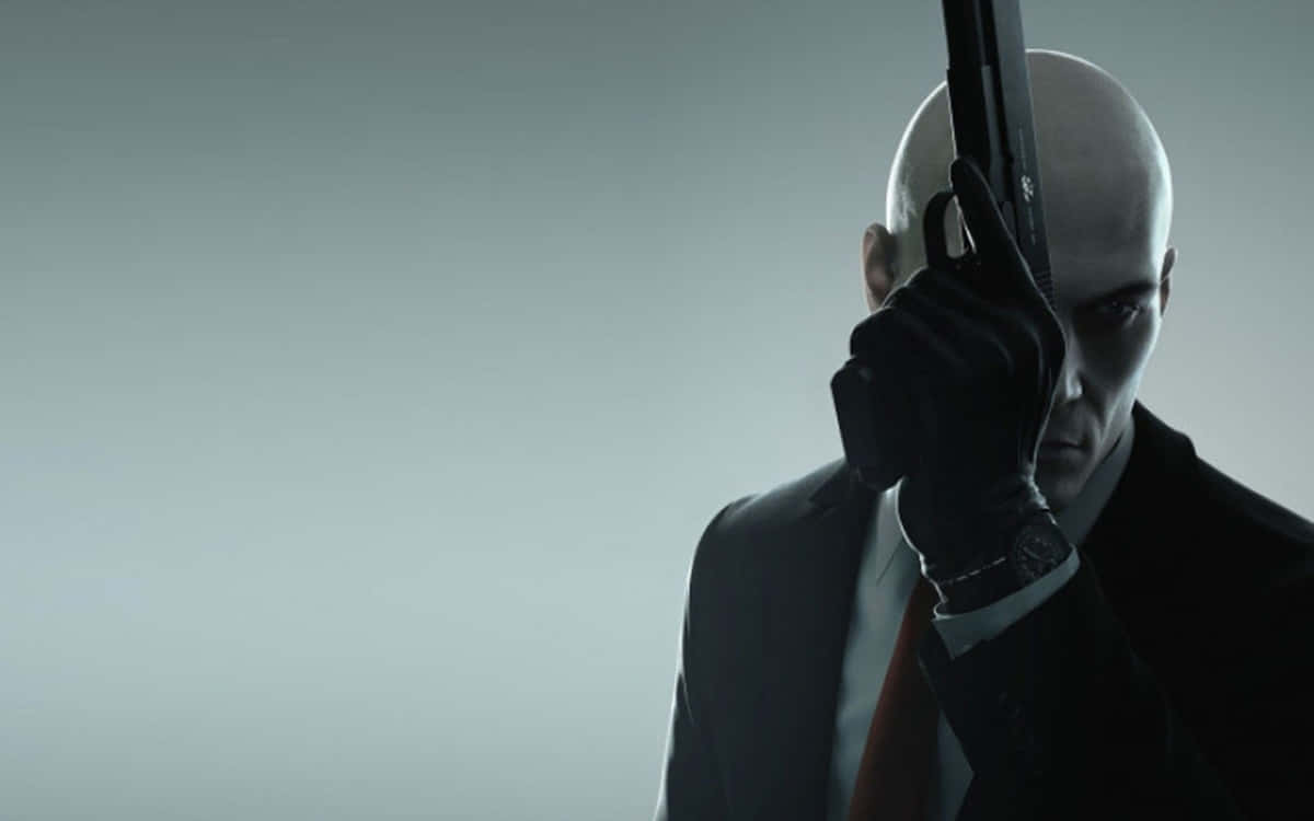 Hitman 3 桌布 壁紙 — 一個光頭刺客穿著黑色西裝，在柔和的灰色背景前將手槍抵住太陽穴。