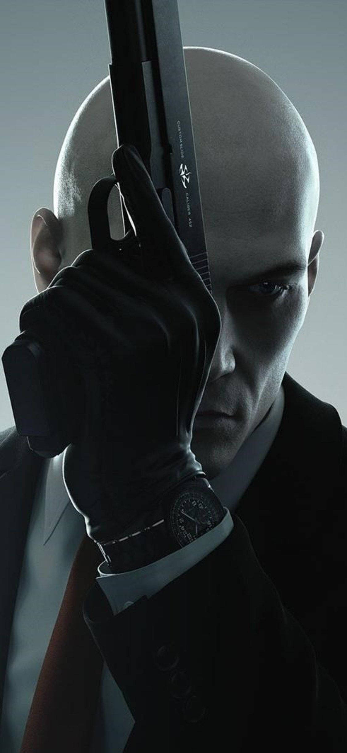 hitman iPhone 桌布 壁紙 — 一個光頭刺客穿著黑色西裝和手套，表情嚴肅地將手槍對準太陽穴，背景為灰色。