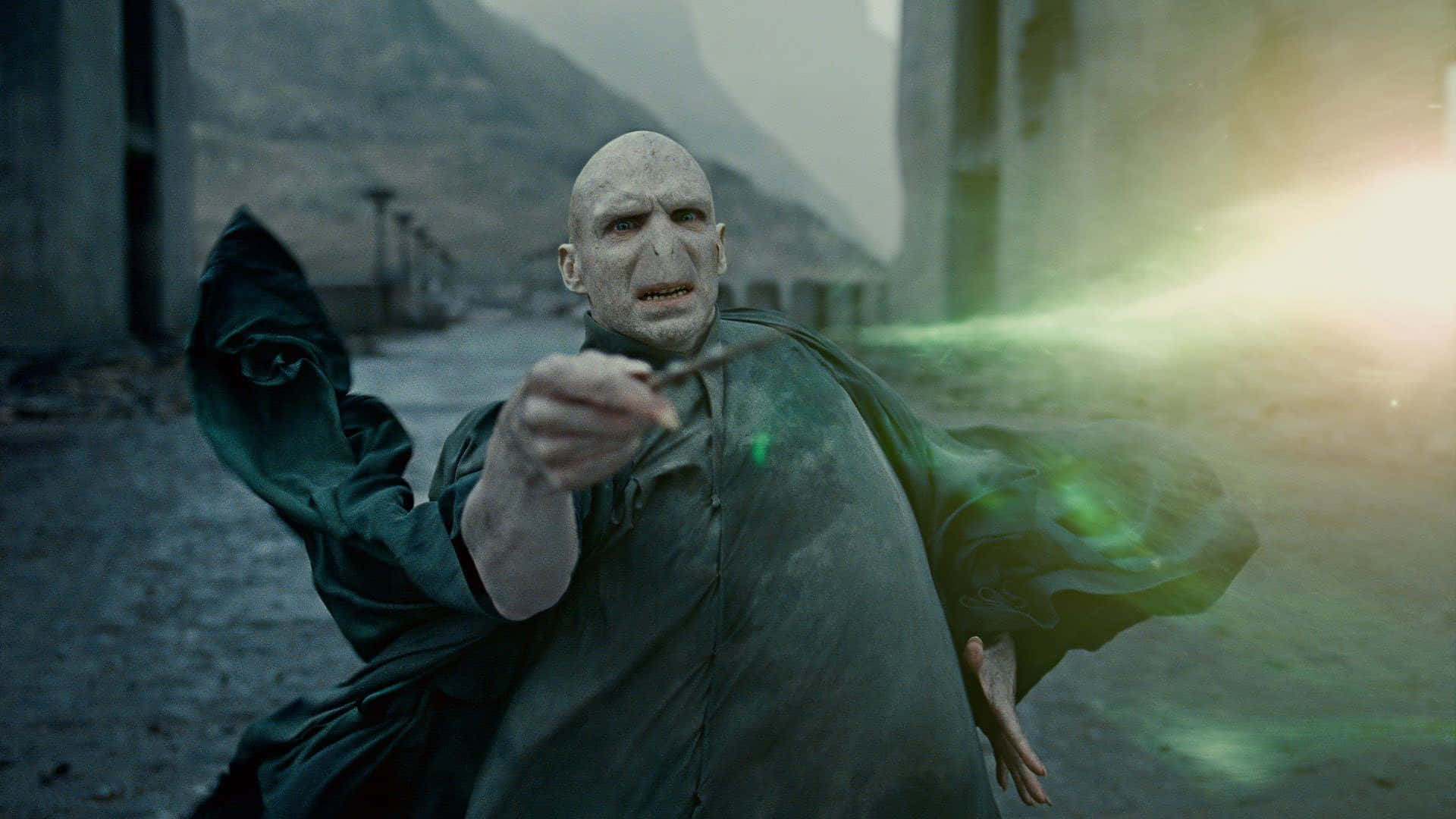 The Battle Of Hogwarts 桌布 壁紙 — 一個光頭巫師穿著黑色長袍，在荒涼的石頭庭院中帶著強烈的憤怒施展綠色法術。