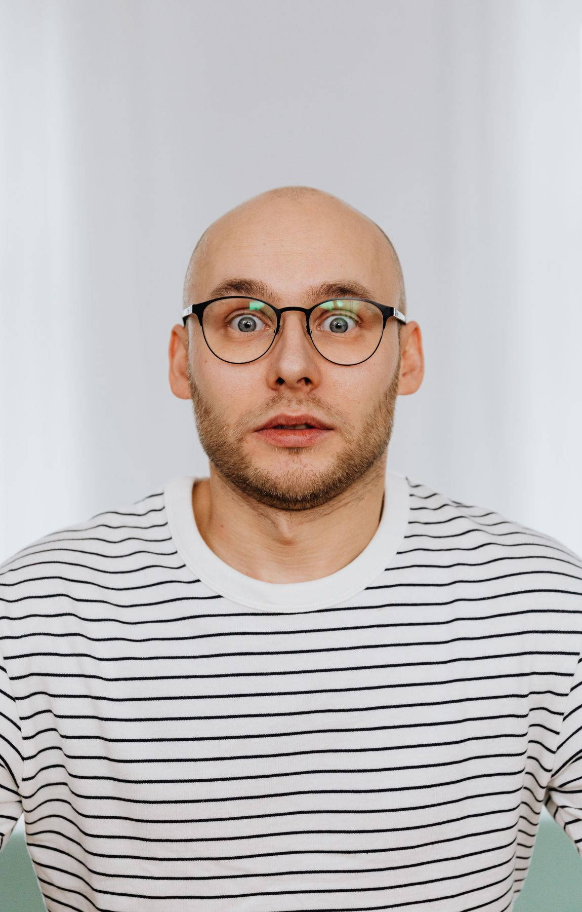 glasses 桌布 壁紙 — 一個光頭戴眼鏡穿條紋衫的男人，在純白背景前震驚地瞪大眼睛。
