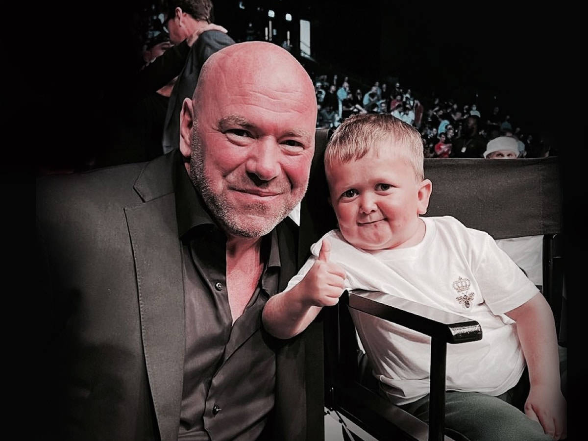 UFC 桌布 壁紙 — 一個光頭男人和一個微笑的幼兒在黑暗的劇院中，後面有觀眾，一起豎起大拇指。
