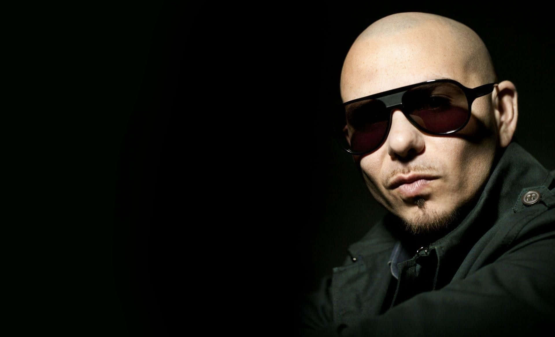 Pitbull 桌布 壁紙 — 一個光頭男人戴著太陽眼鏡和山羊鬍，在黑暗背景下強烈凝視。