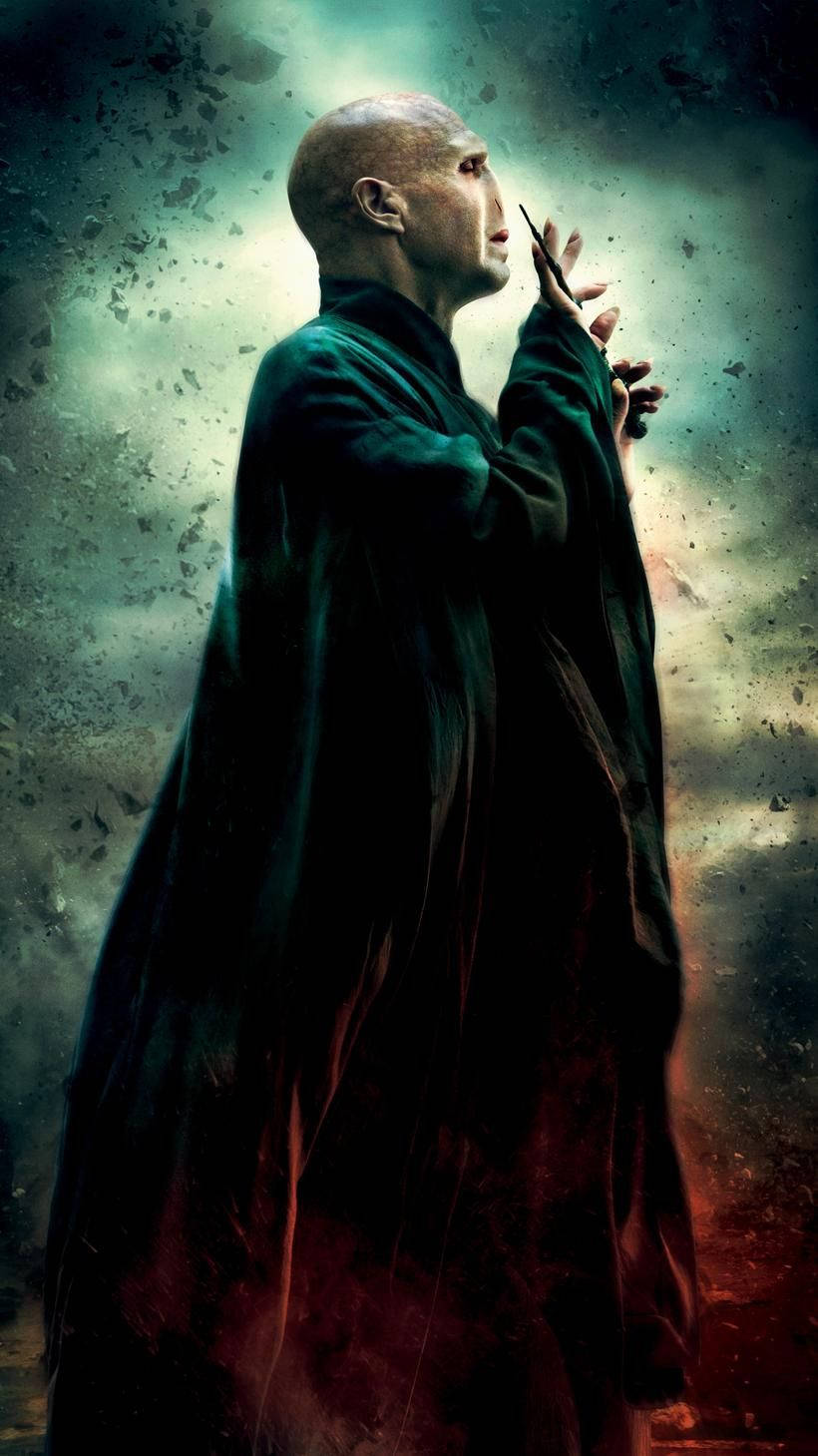 voldemort 桌布 壁紙 — 一個光頭男人穿著深綠色長袍，站在風暴中充滿碎片的天空，腳下有發光的紅色點綴。