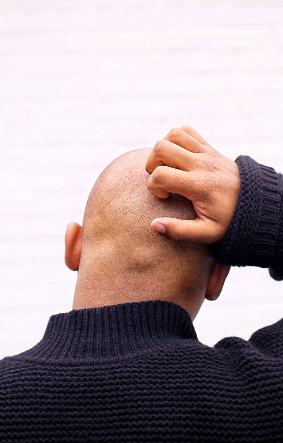 scratching head 桌布 壁紙 — 一個光頭男人穿著深色毛衣，在純白色背景前抓頭後部。