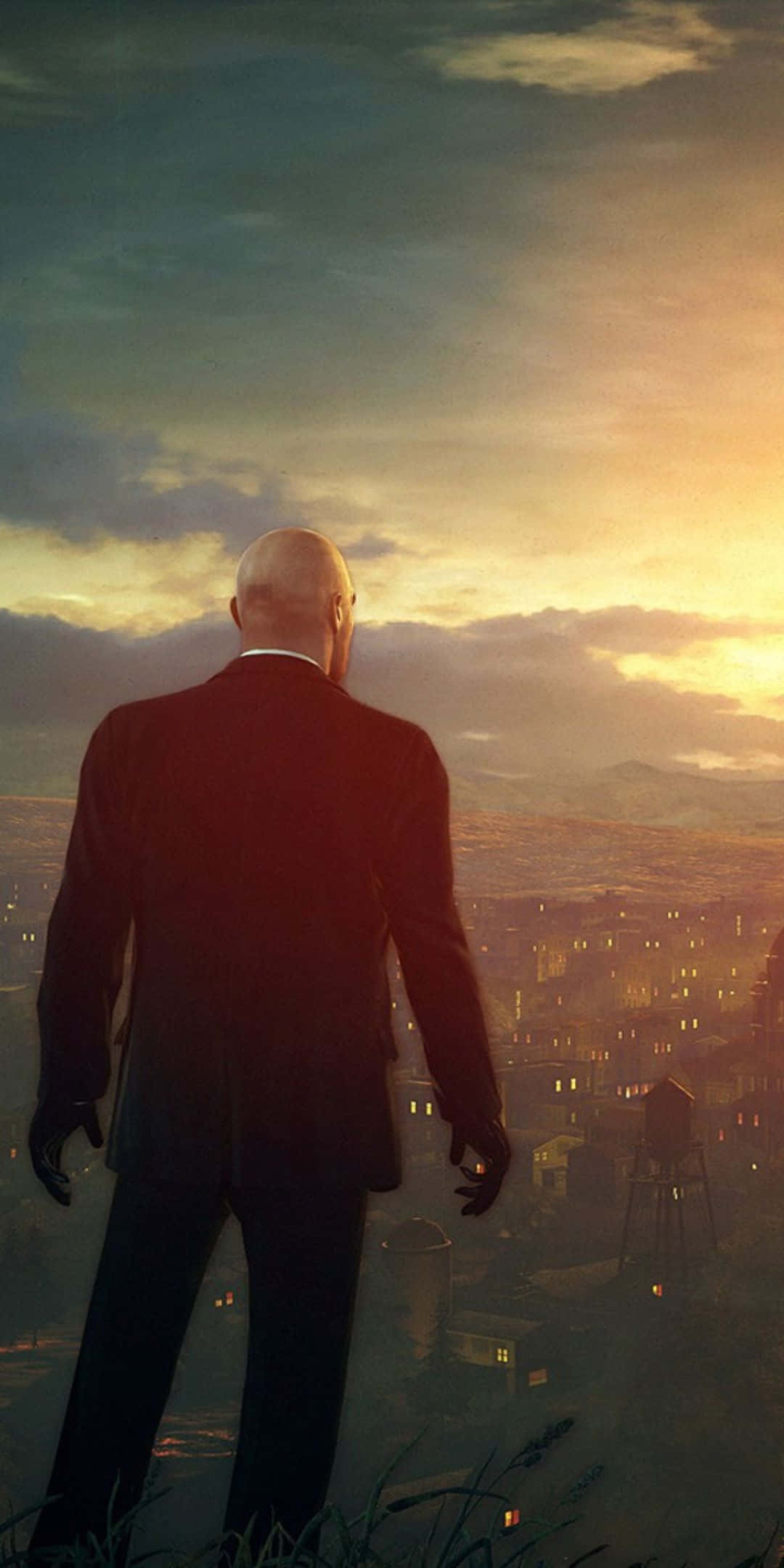 Pixel 3 Hitman Absolution 桌布 壁紙 — 一個光頭男人穿著深色西裝，站在山丘上，俯瞰著夕陽下溫暖金色光芒中蔓延的城市。