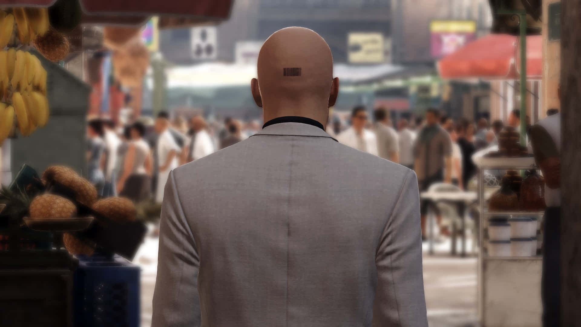 Hitman Desktop 桌布 壁紙 — 一個光頭男人穿著灰色西裝，沿著一條擺滿水果攤和人群的繁華城市街道走開。