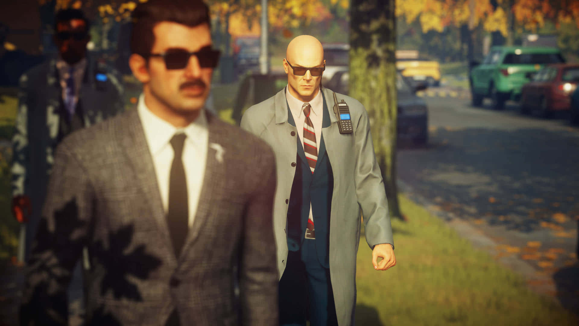 1920x1080 Hitman 2 桌布 壁紙 — 一個光頭男人穿著灰色風衣和太陽眼鏡，走在兩旁種滿樹木的街道上，周圍有秋天的落葉飄落。