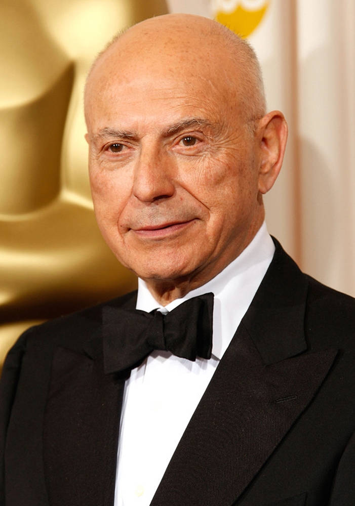 oscars 桌布 壁紙 — 一個光頭男人穿著黑色禮服和領結，對著鏡頭微笑，身後有一個金色的奧斯卡獎座的特寫肖像。