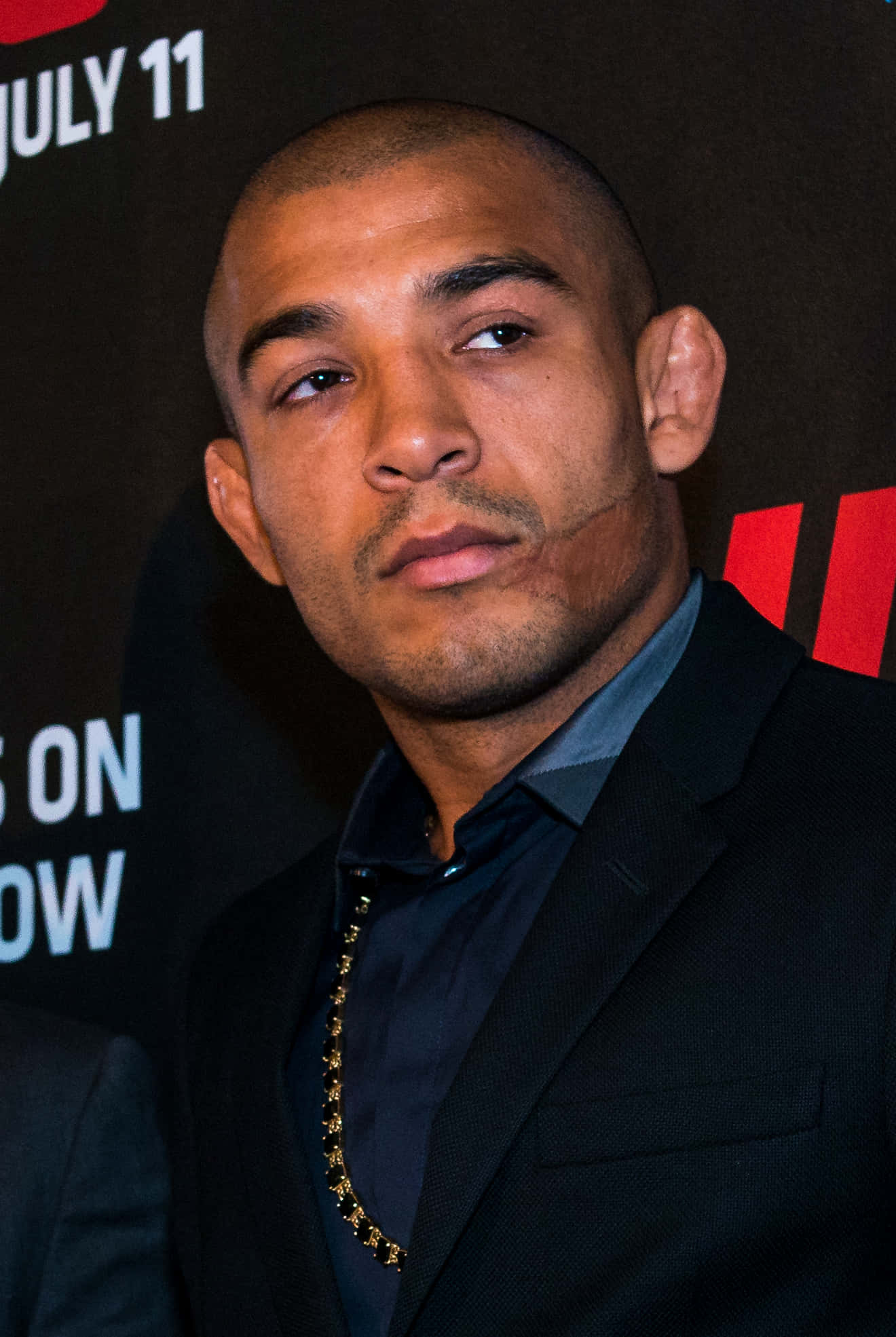 UFC 桌布 壁紙 — 一個光頭男人穿著黑色西裝和戴著金鏈，在推廣活動中望向鏡頭外的特寫肖像。