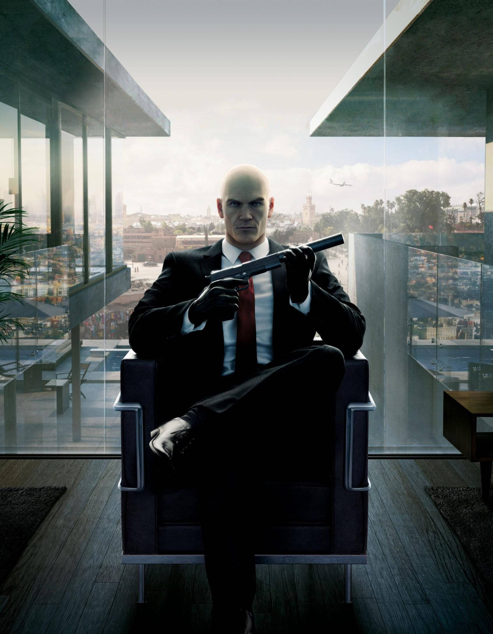 hitman iPhone 桌布 壁紙 — 一個光頭男人穿著黑色西裝和紅色領帶，坐在現代椅子上，手持槍支，透過玻璃牆俯瞰城市景觀。