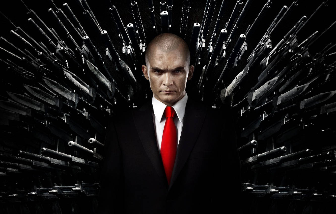 Hitman Black 桌布 壁紙 — 一個光頭男人穿著黑色西裝和紅色領帶，站在中央，目光嚴厲，周圍是放射狀排列的武器，背景為黑色。