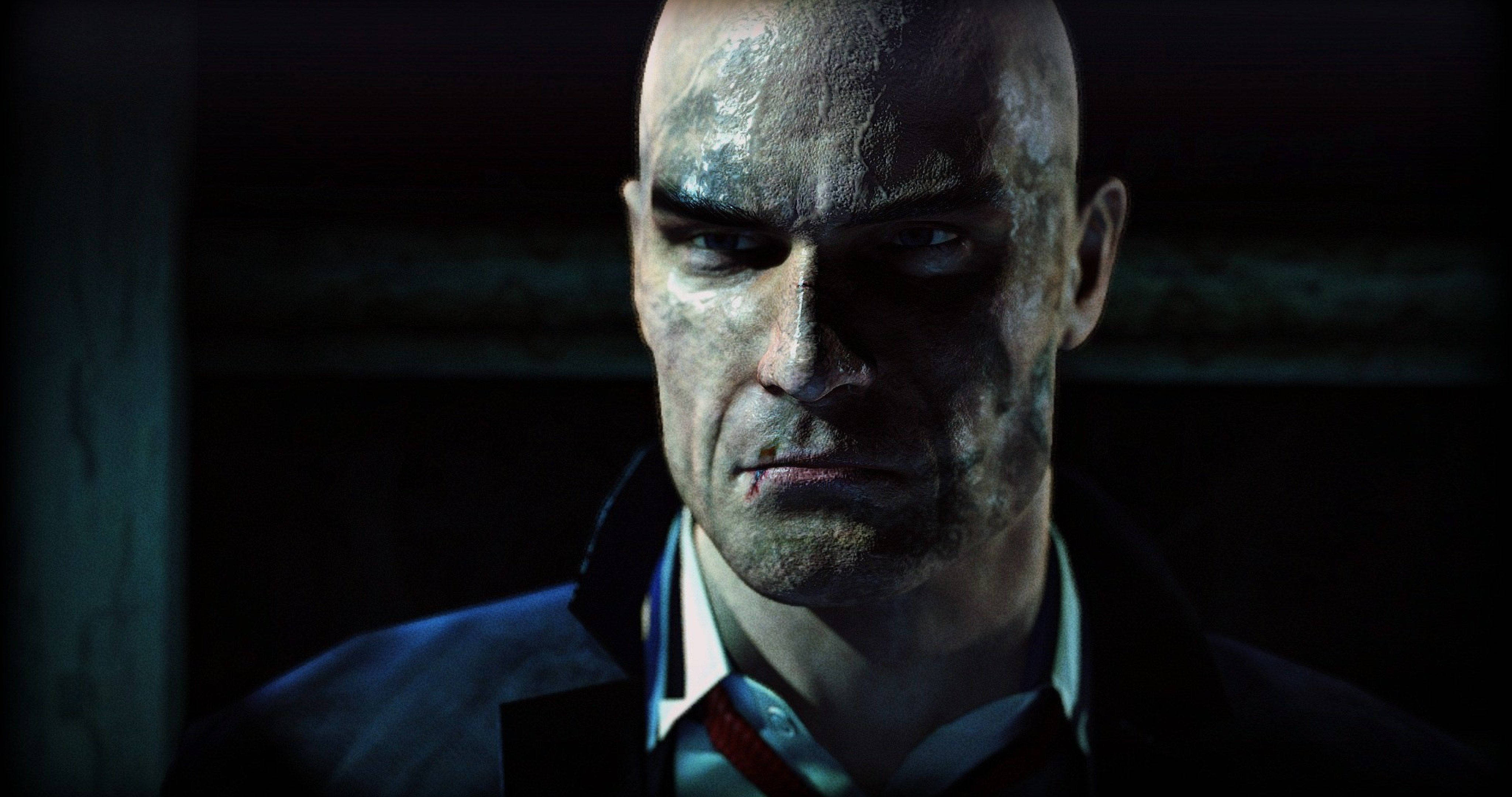 Hitman Absolution 桌布 壁紙 — 一個光頭男子，表情嚴峻，臉上沾滿污垢，在昏暗燈光下凝視著。