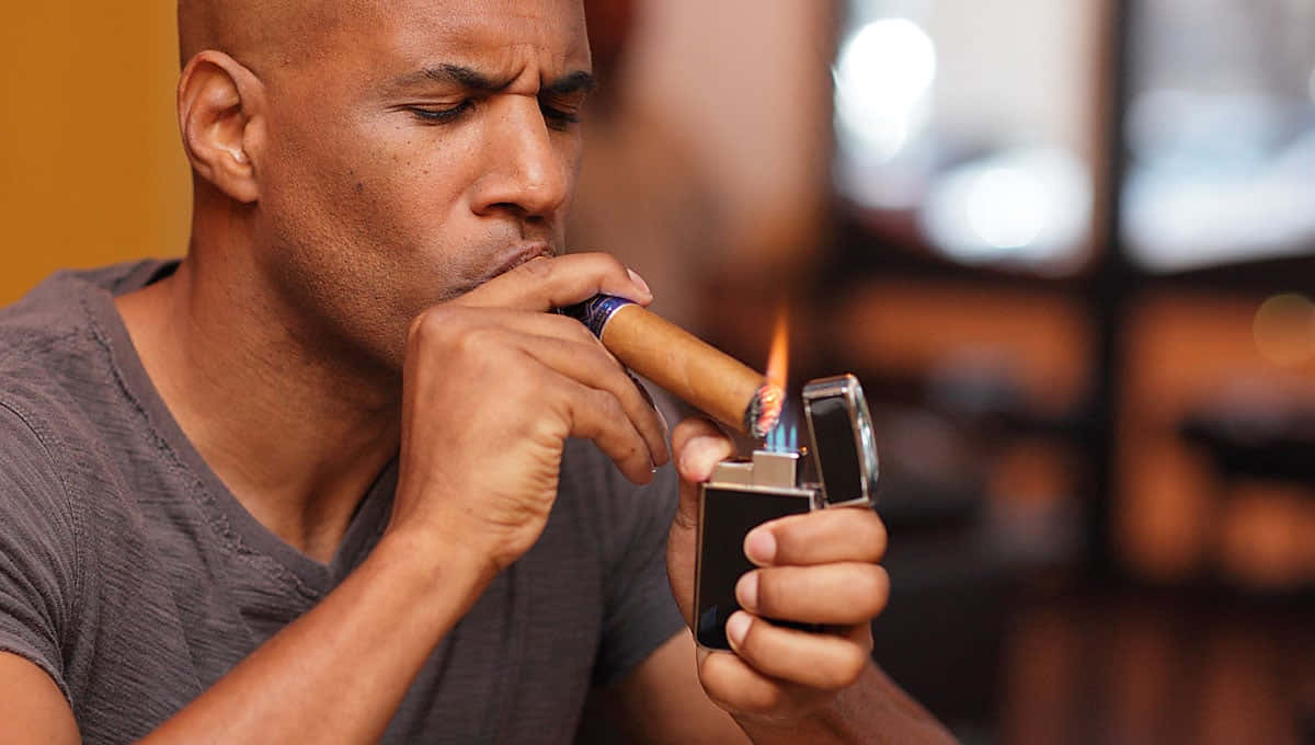 lighter 桌布 壁紙 — 一個光頭男子在溫暖的室內環境中用銀色打火機點燃雪茄。