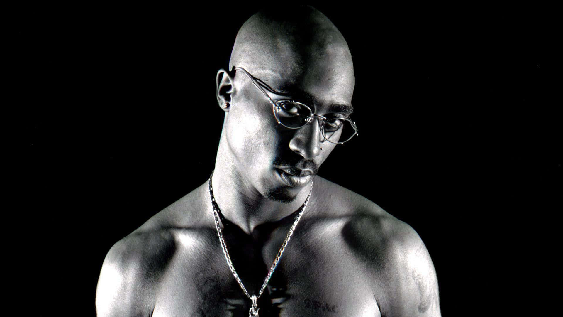 tupac 桌布 壁紙 — 一個光頭男子戴著眼鏡和鏈條項鍊，在深色背景下的黑白肖像。